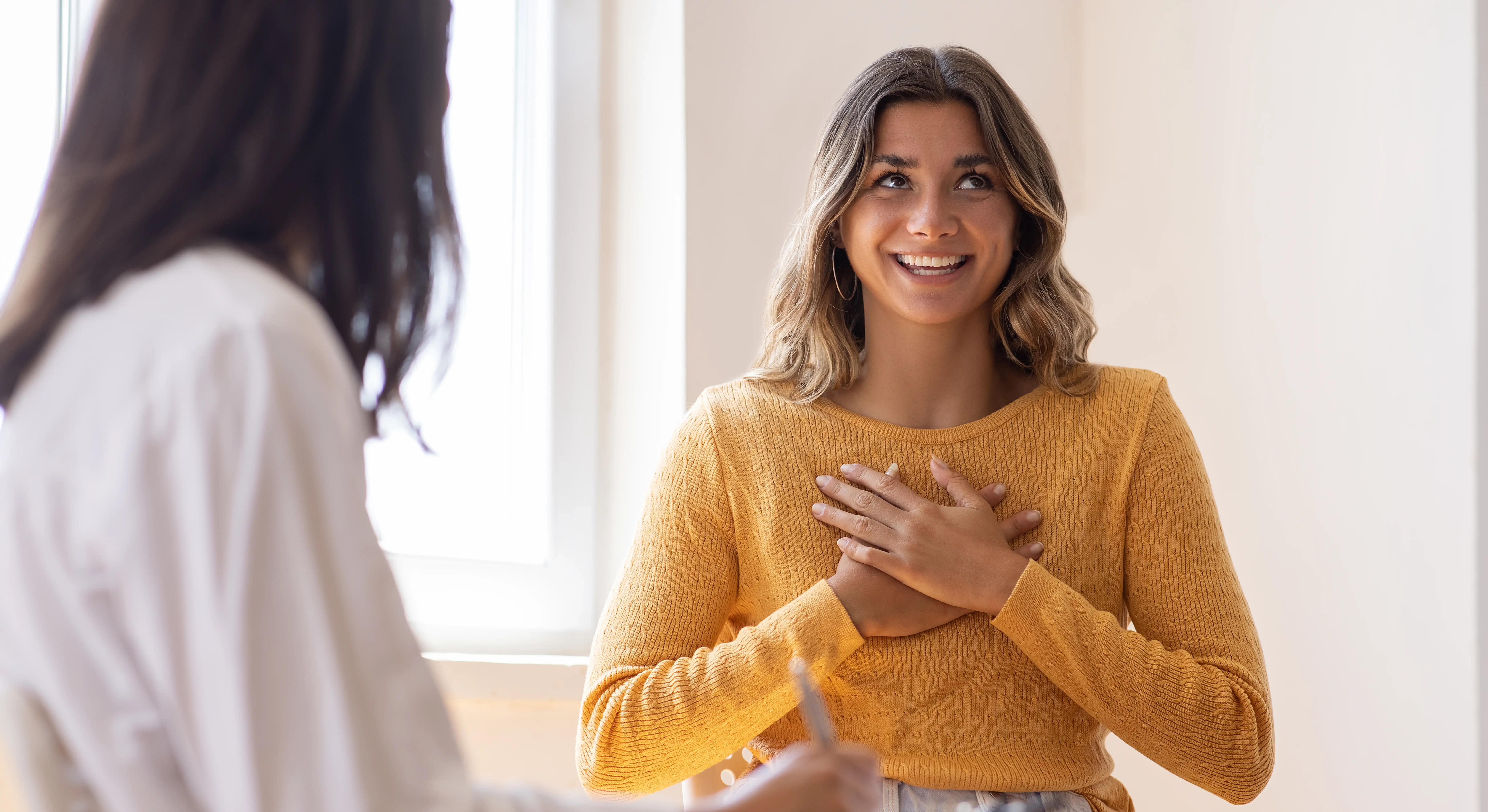 A women smiles and presses her hands to her chest in relief as she speaks to her doctor