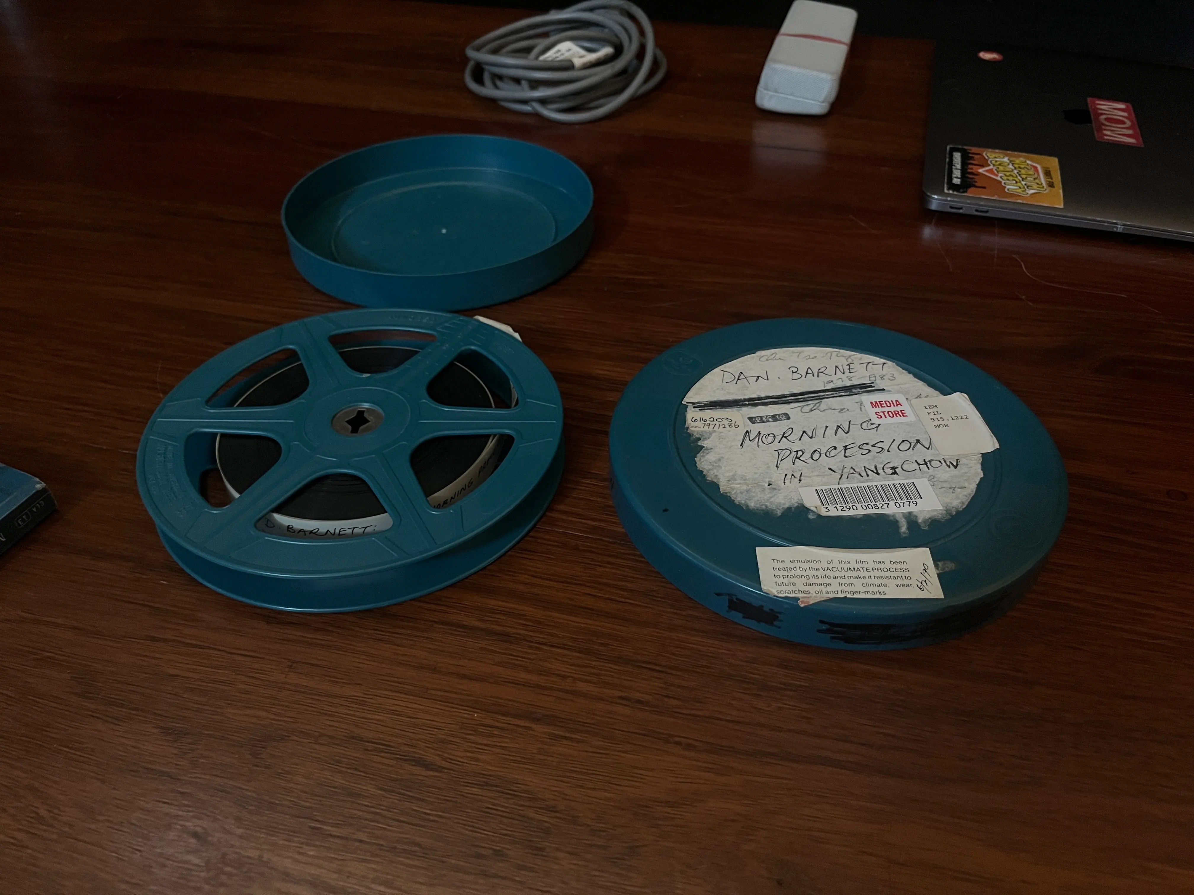 An image of the an old looking 16mm film canister sitting on a table. The film canister is titled Morning Procession in Yangchow