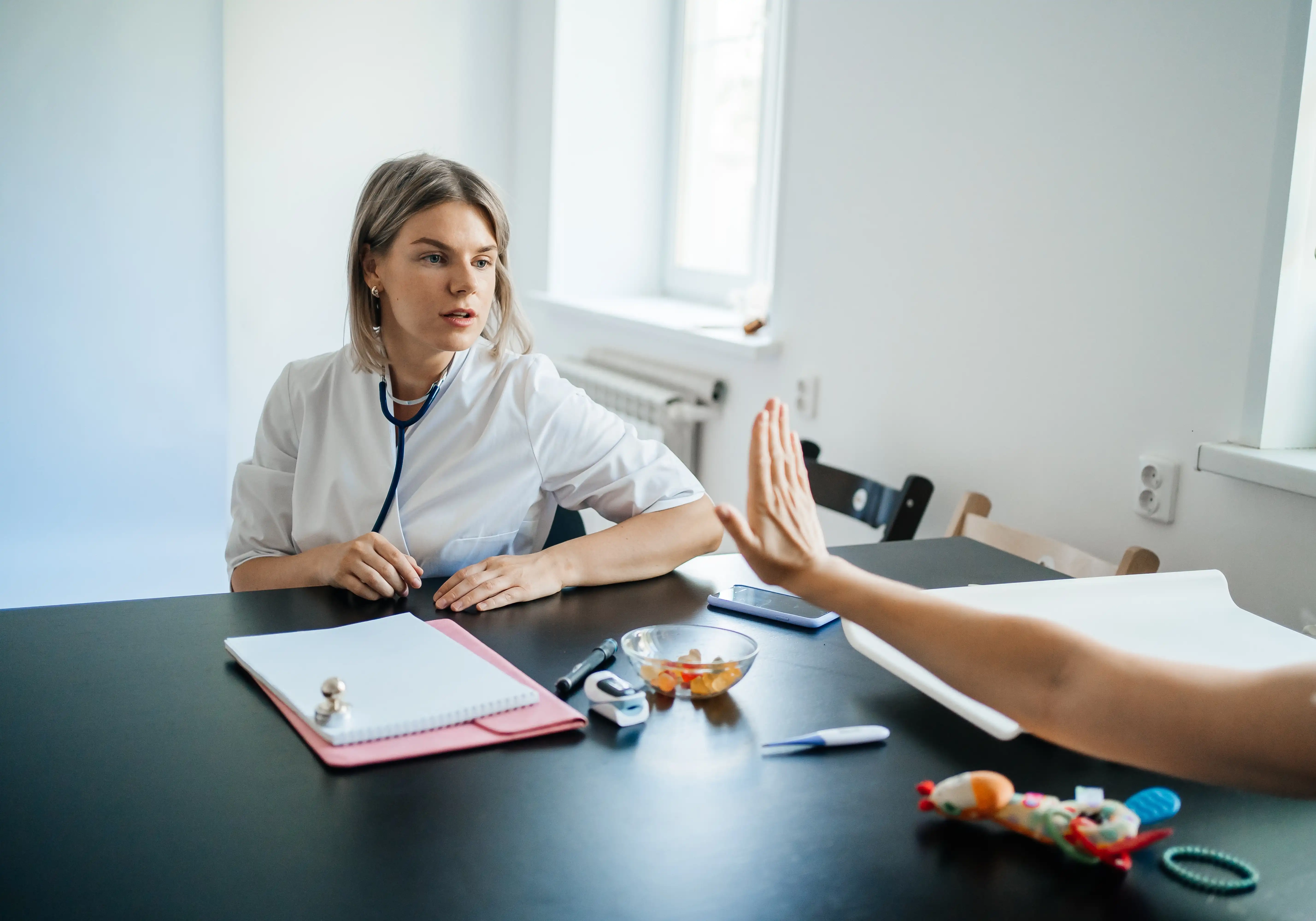 Patient extends their arm over the desk with a flat palm to indicate 'stop' to their doctor