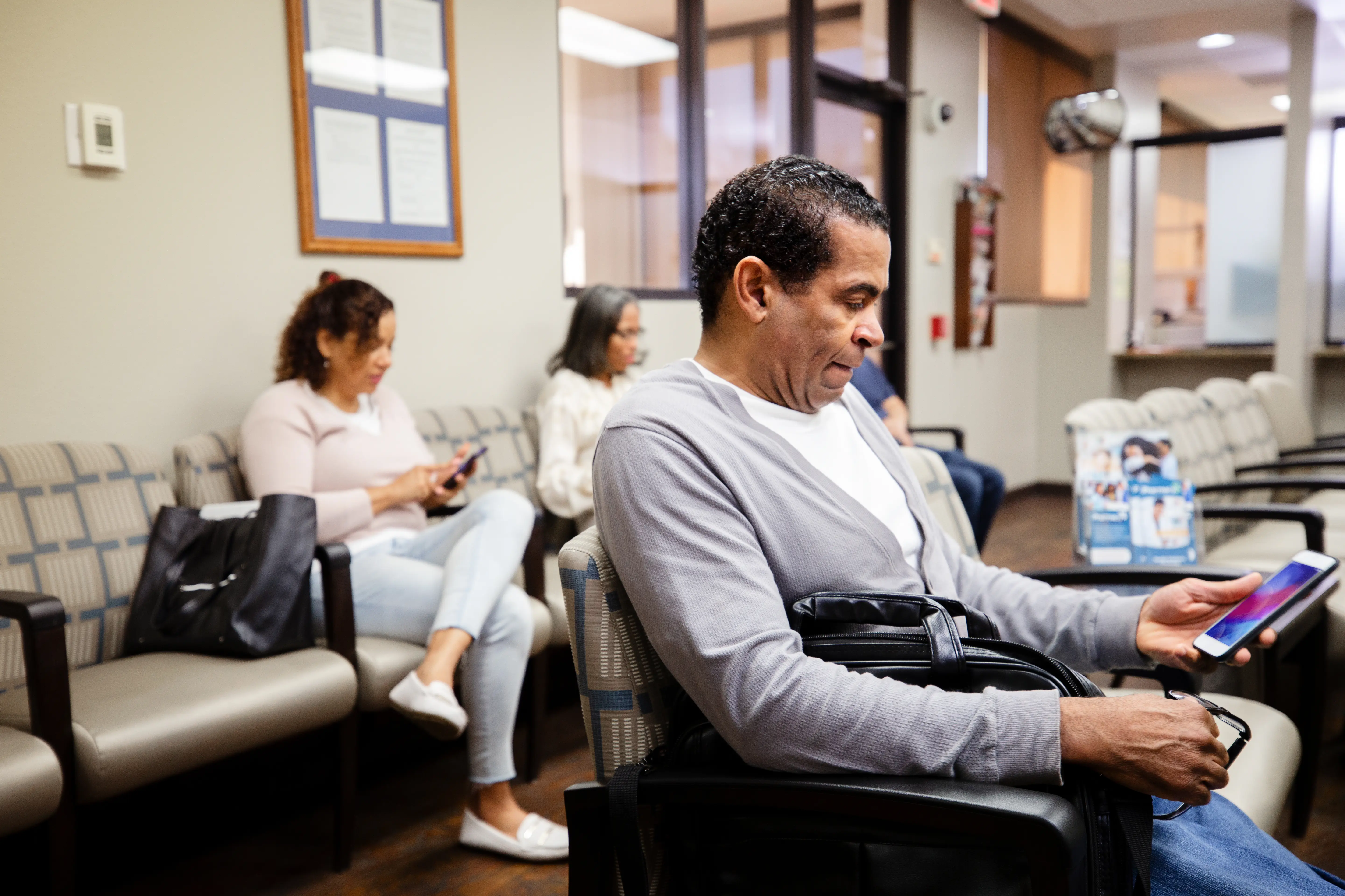 A man looking at his smart phones while sitting in doctor's waiting room