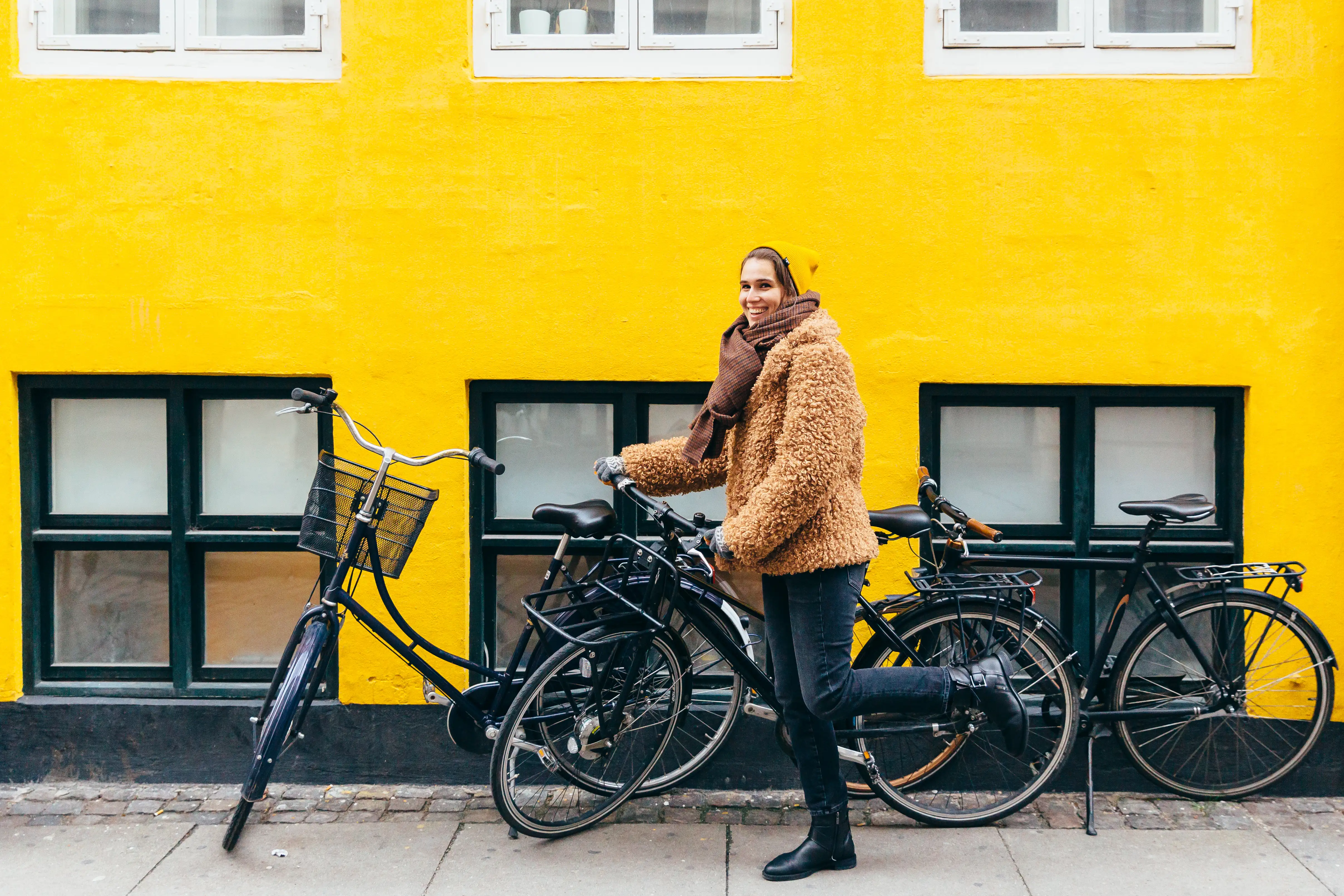 Happy young smiling woman with bicycle against yellow wall in Copenhagen