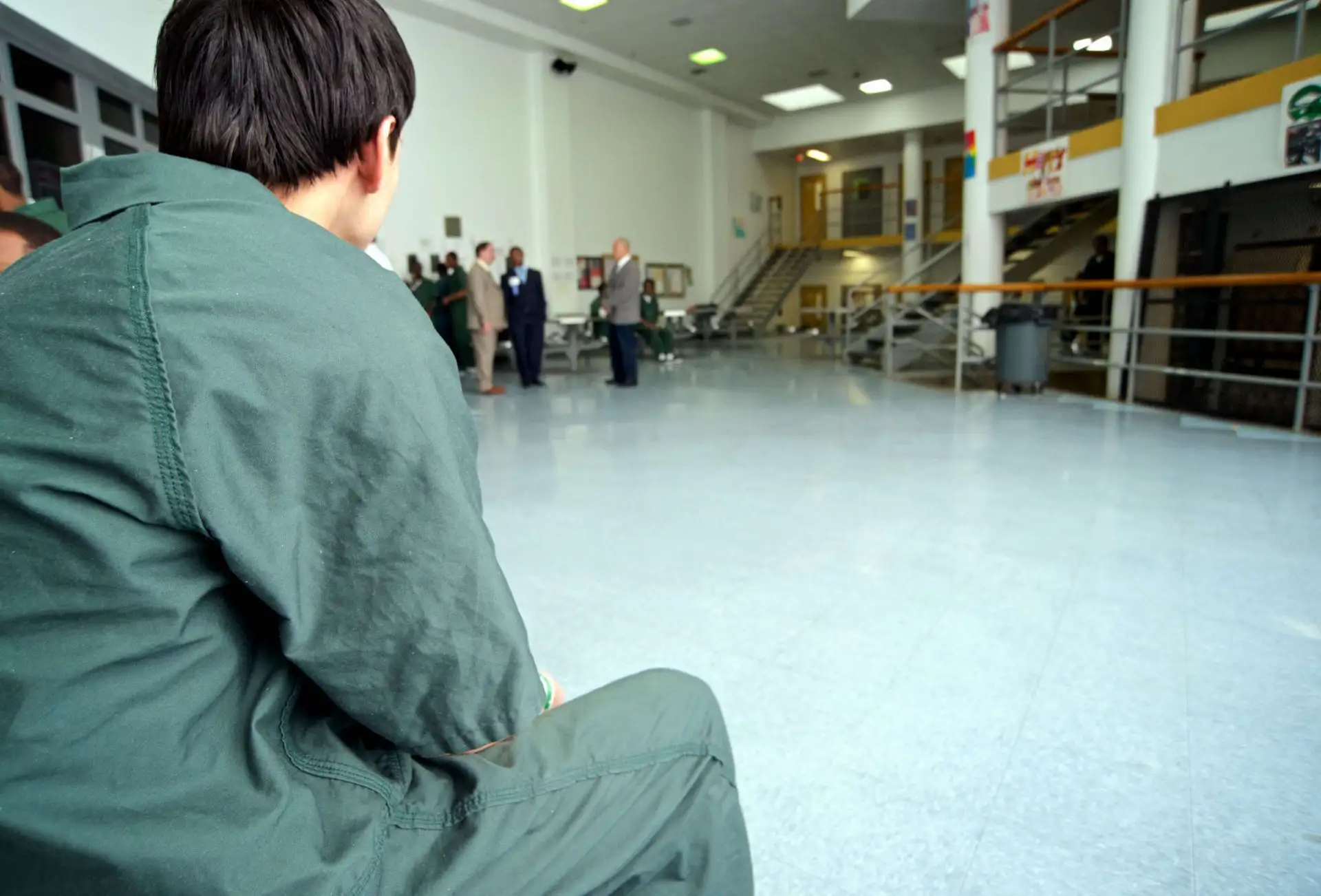 A young person in a detention centre photographed over the shoulder looking into a common area