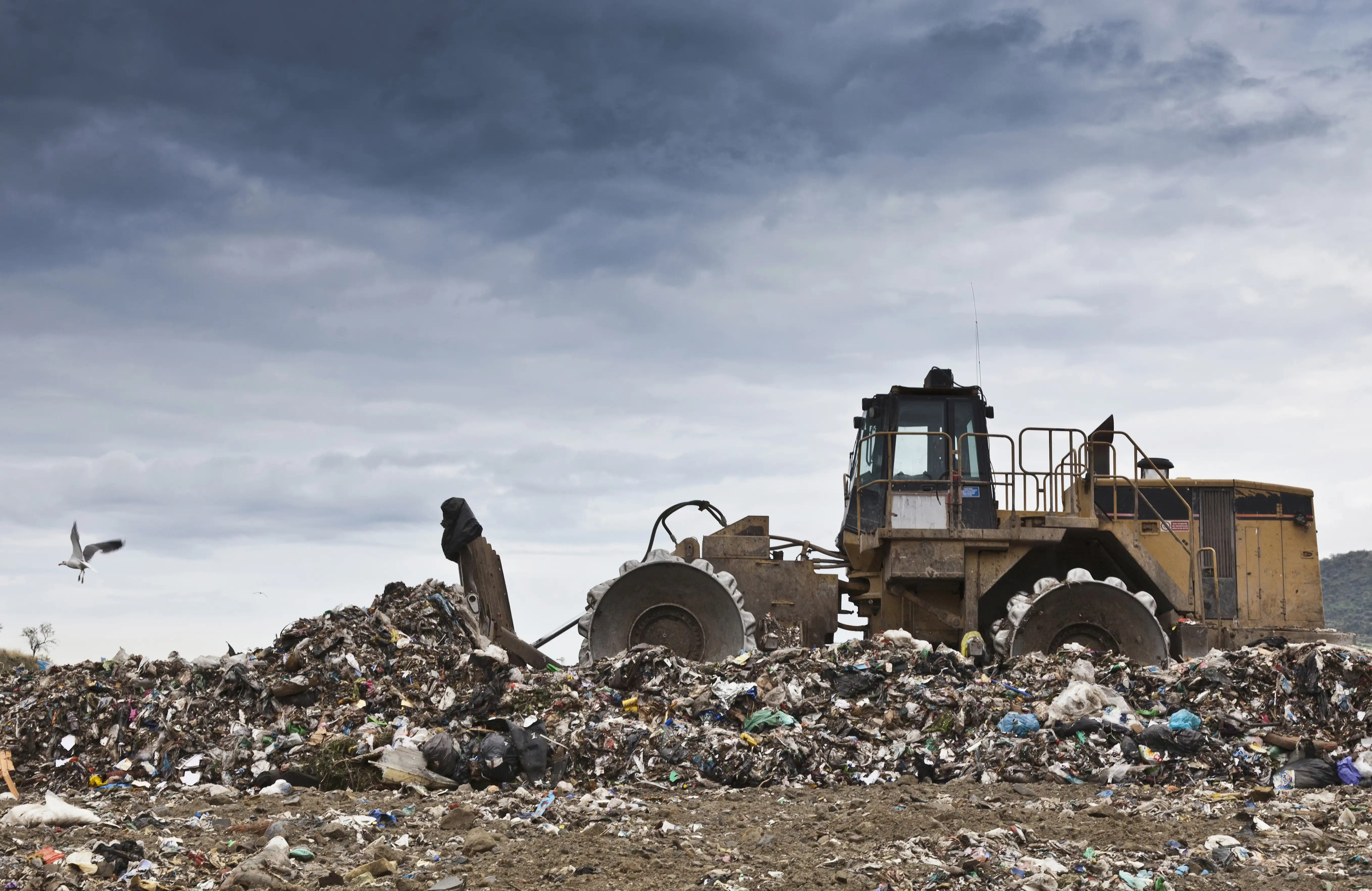 A truck moving a big stack of trash at a landfill site