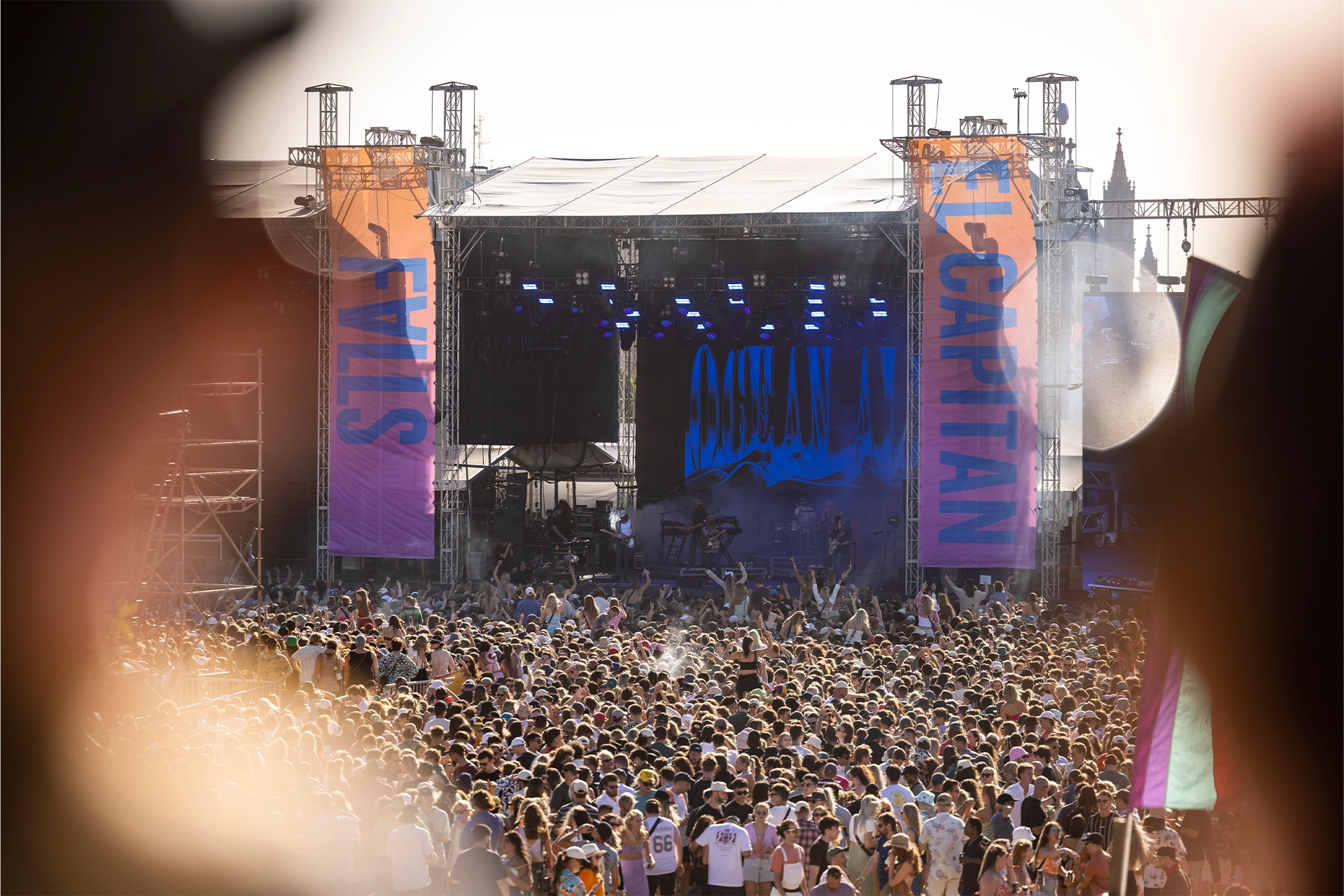 Daytime crowd at a music festival with a large stage in the background