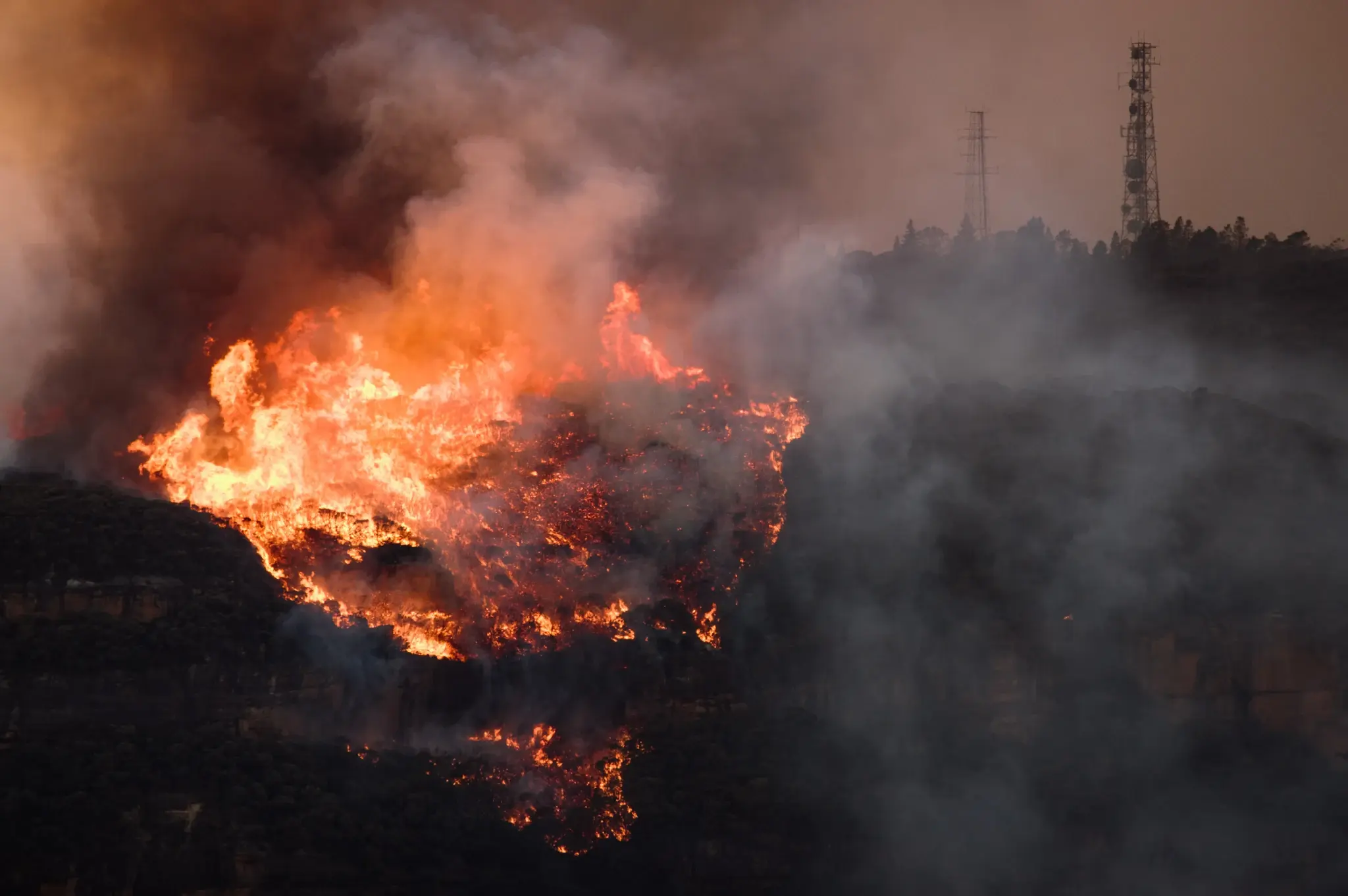 A wildfire approaching power lines on a hill