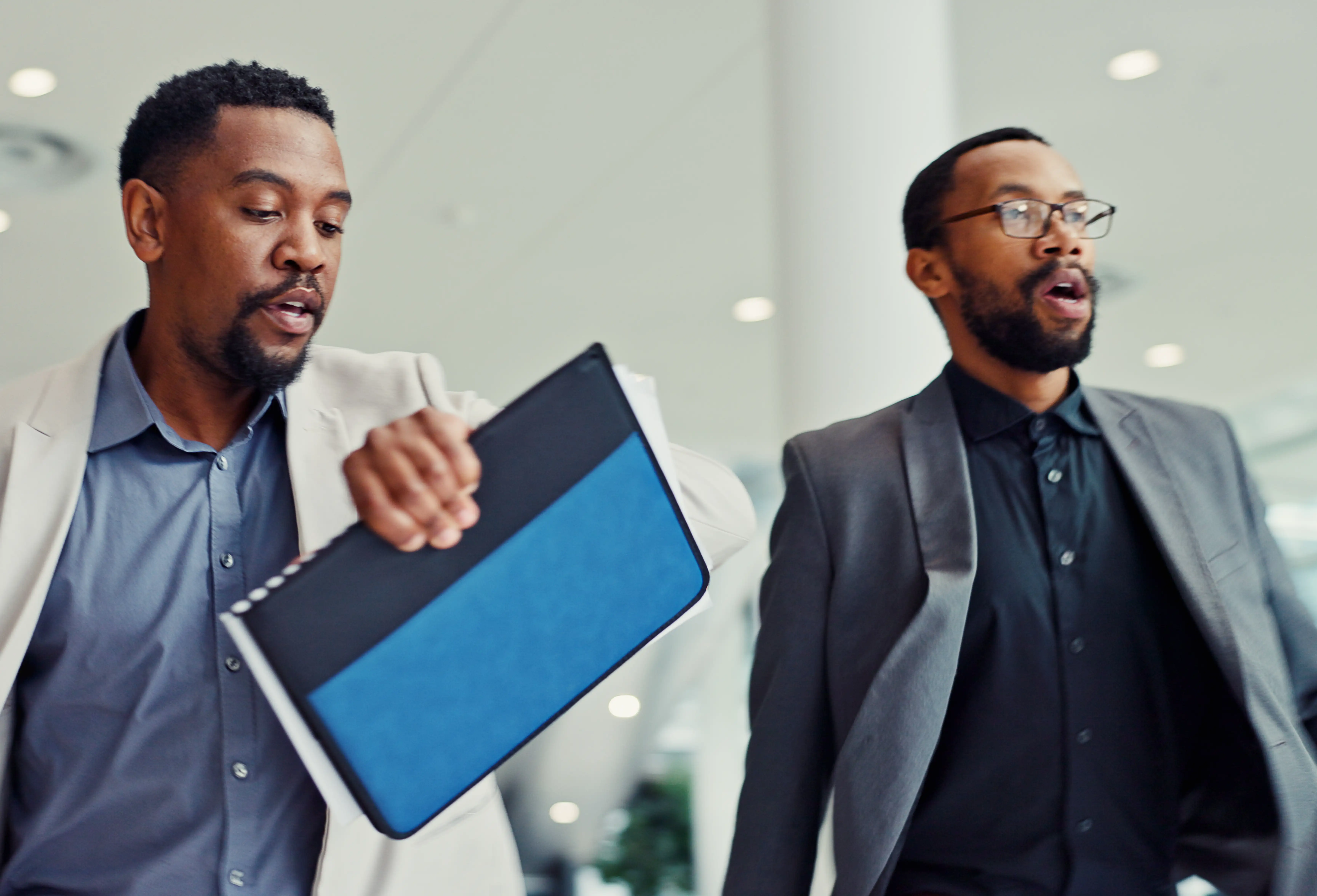 Two businessmen, one checking watch and rushing into a lobby with documents
