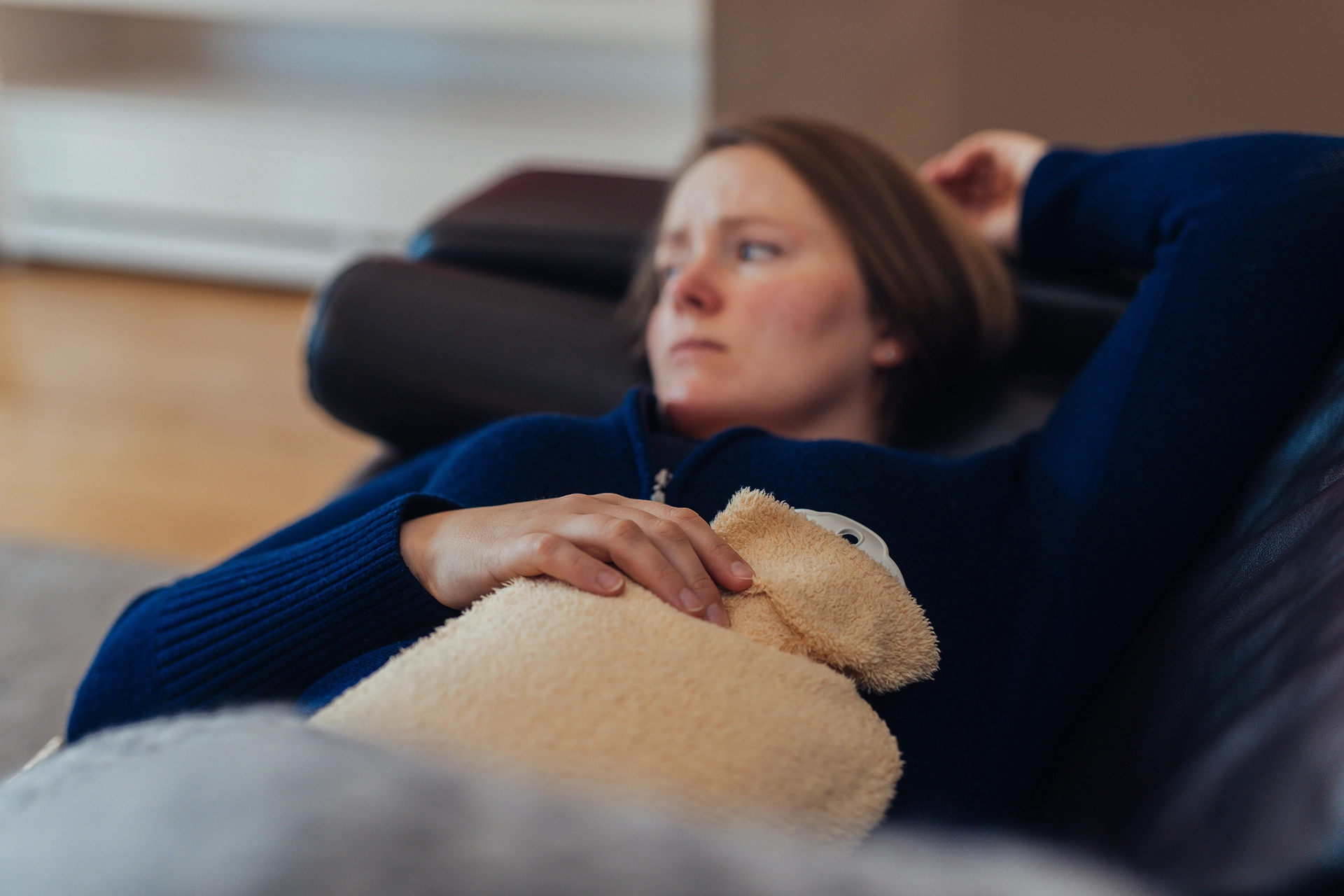 Woman lying in discomfort with waterbottle over belly