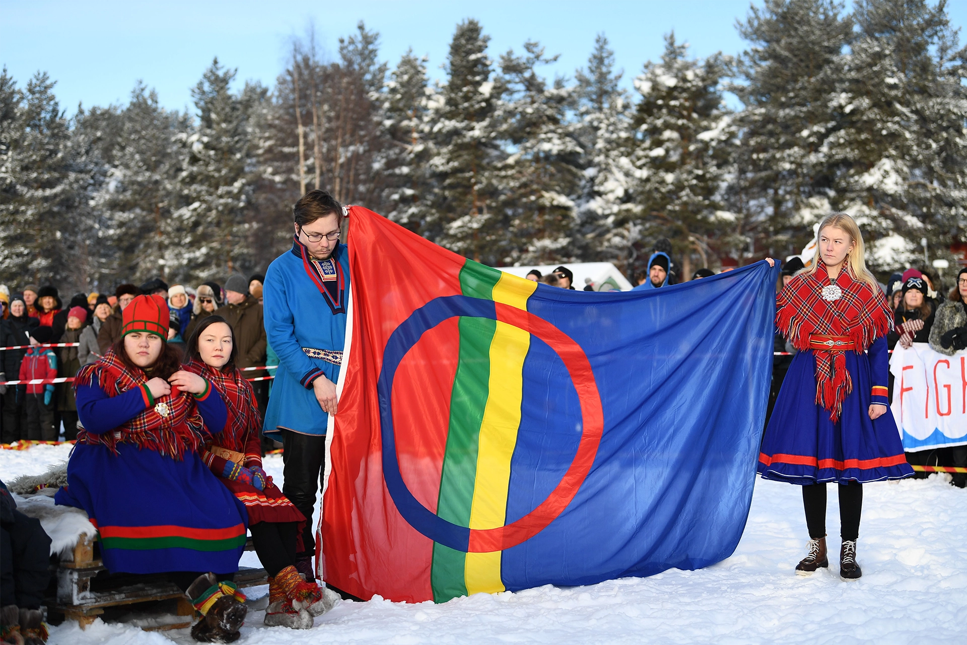 Group of people wearing traditional Sami dress and holding Sami flag in snowy landscape