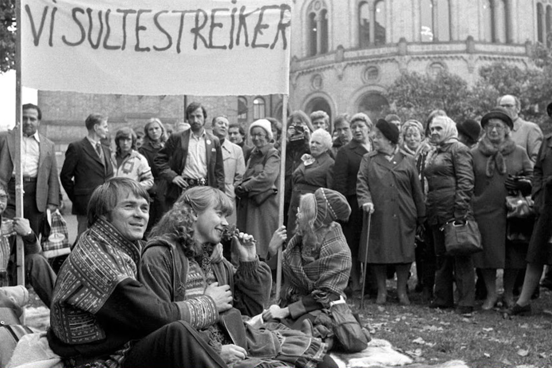 Black and white photo of Sami group sitting on ground outdoors during a protest