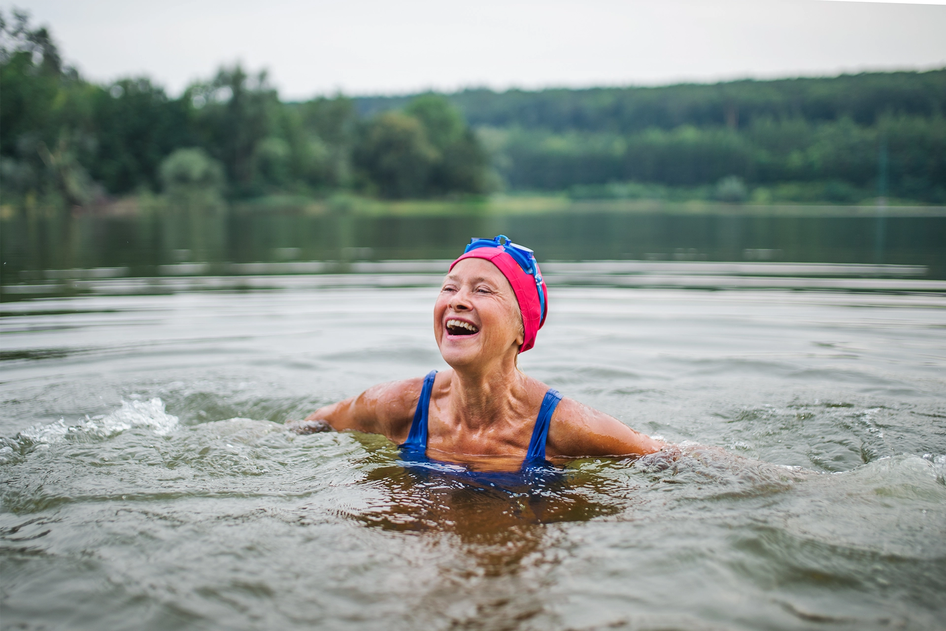 Senior woman wearing swimming cap swimming and smiling in outdoor lake