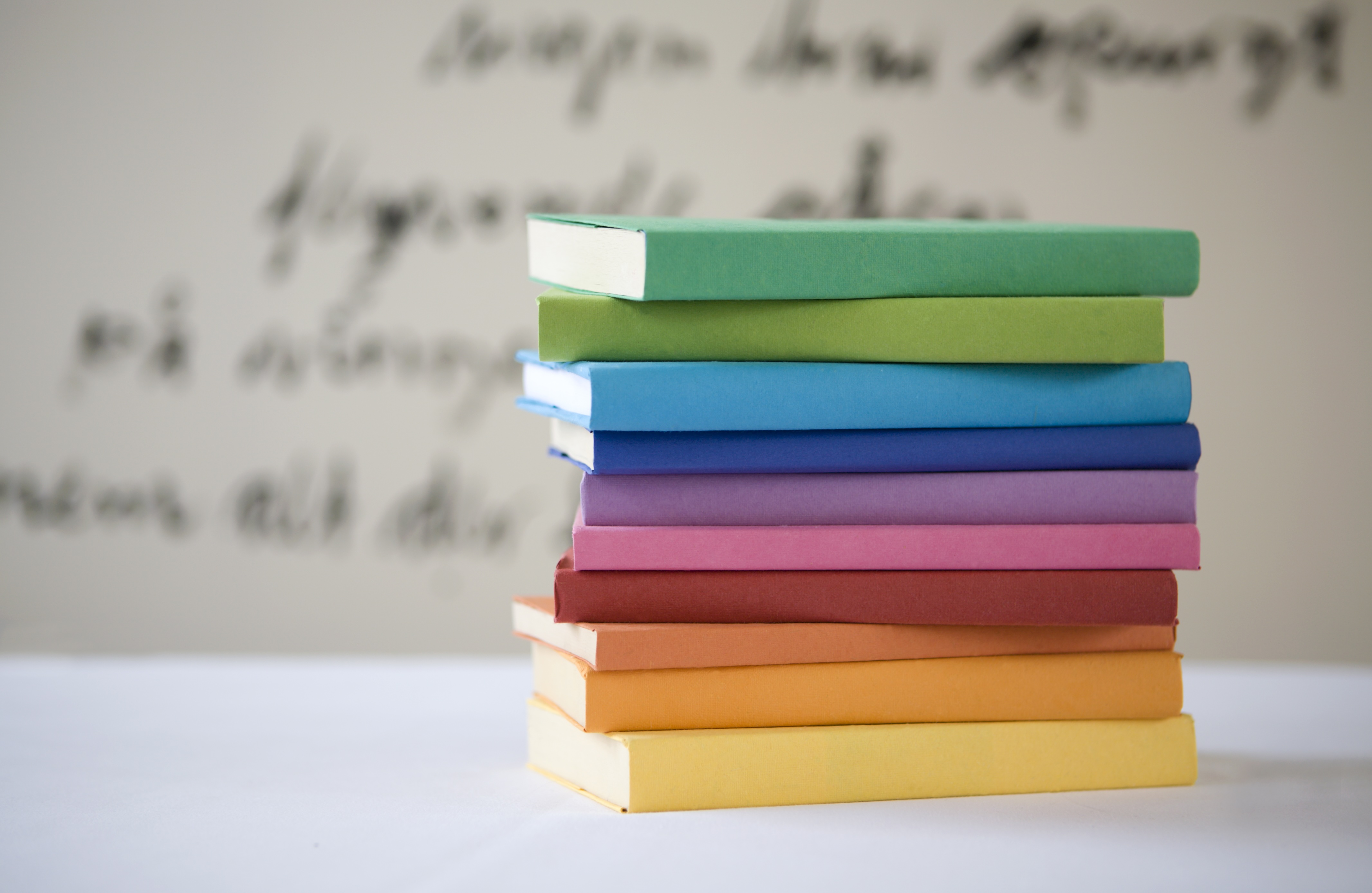 Rainbow pile of books with writing in background