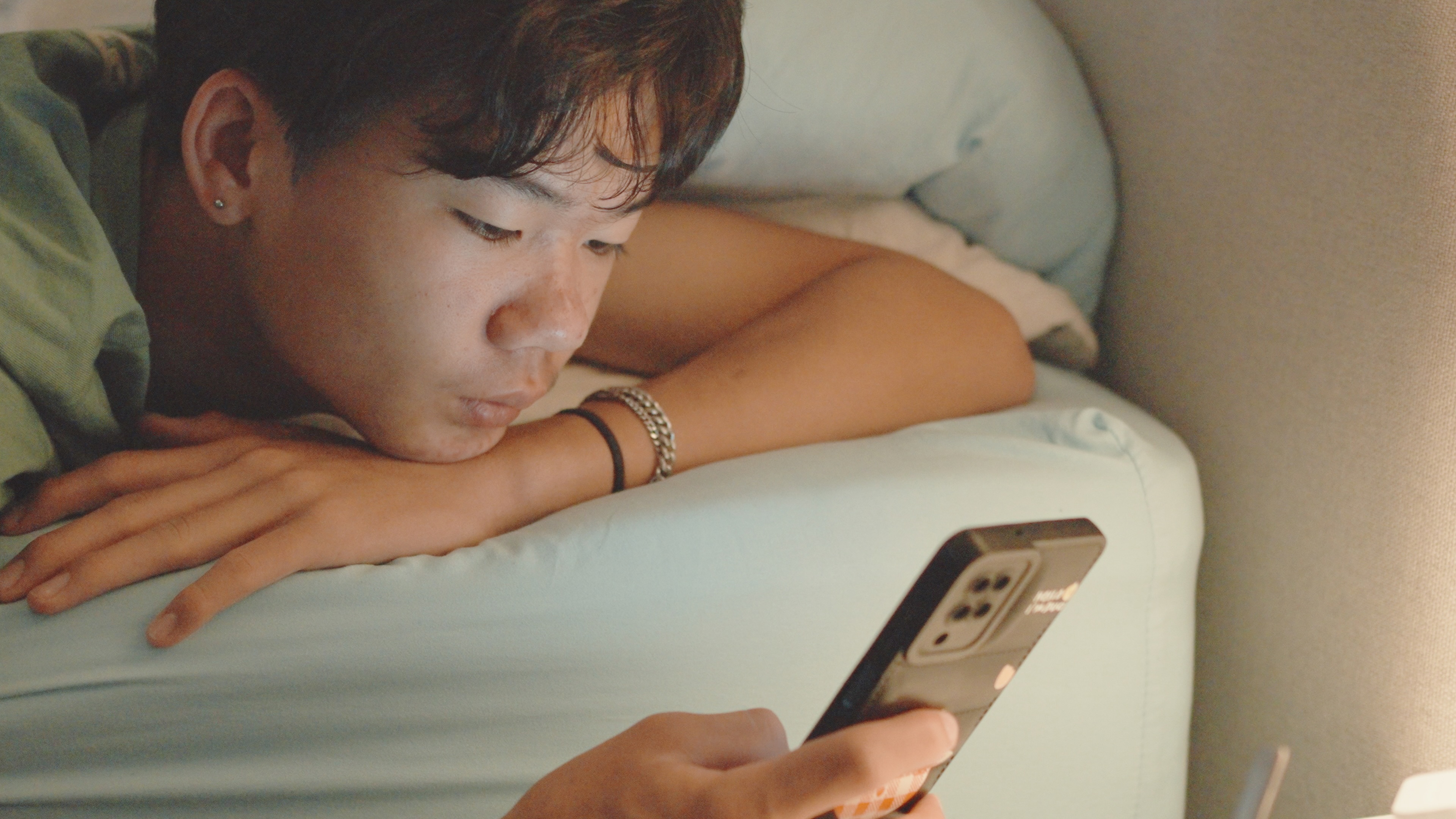 Teen boy lying on bed with phone looking down