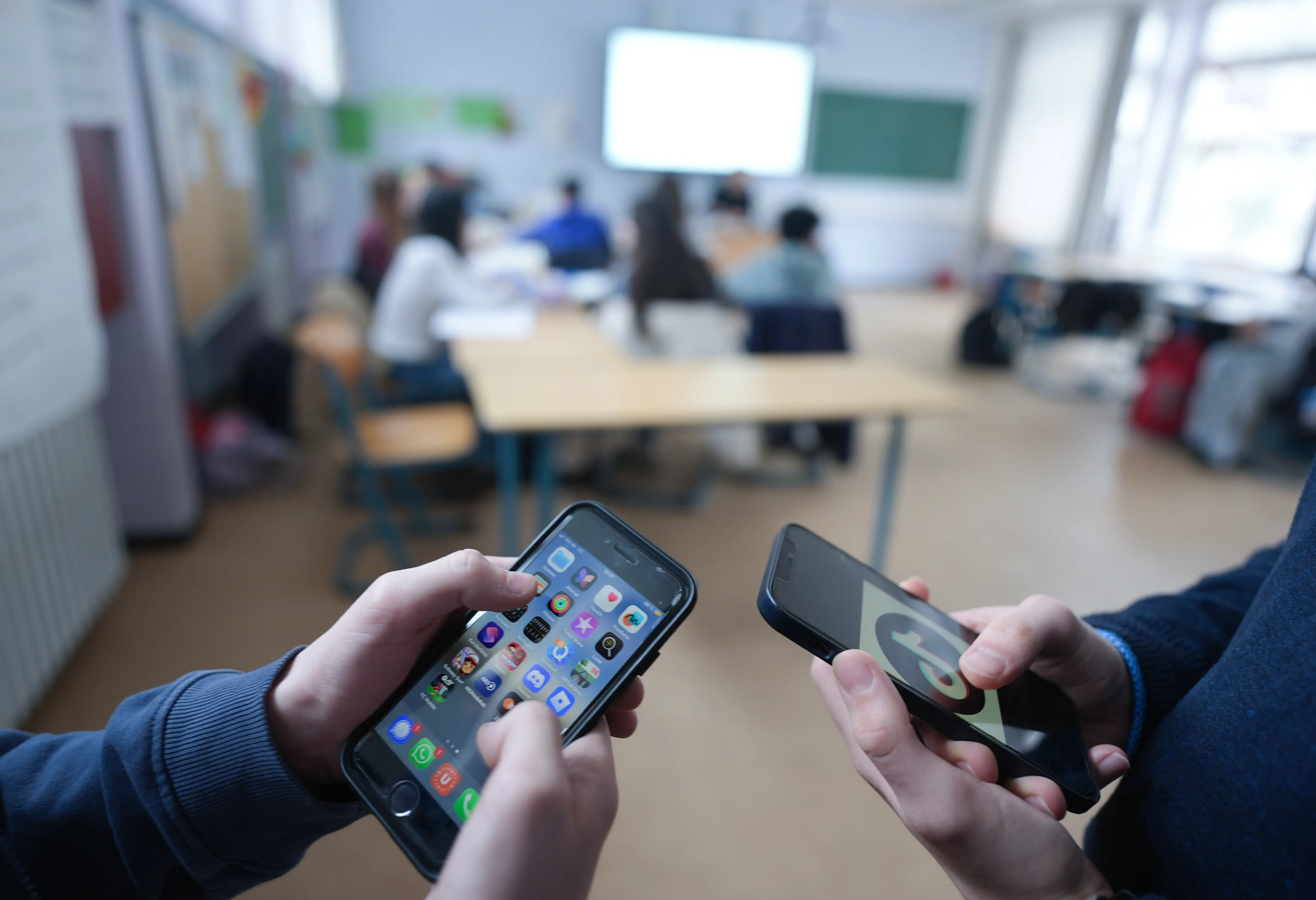 Two students stand in a classroom looking at the social media apps on their smartphones
