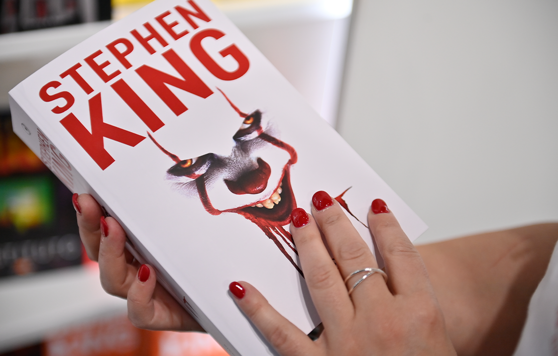Woman's hands holding a white book with a creepy clown on the cover