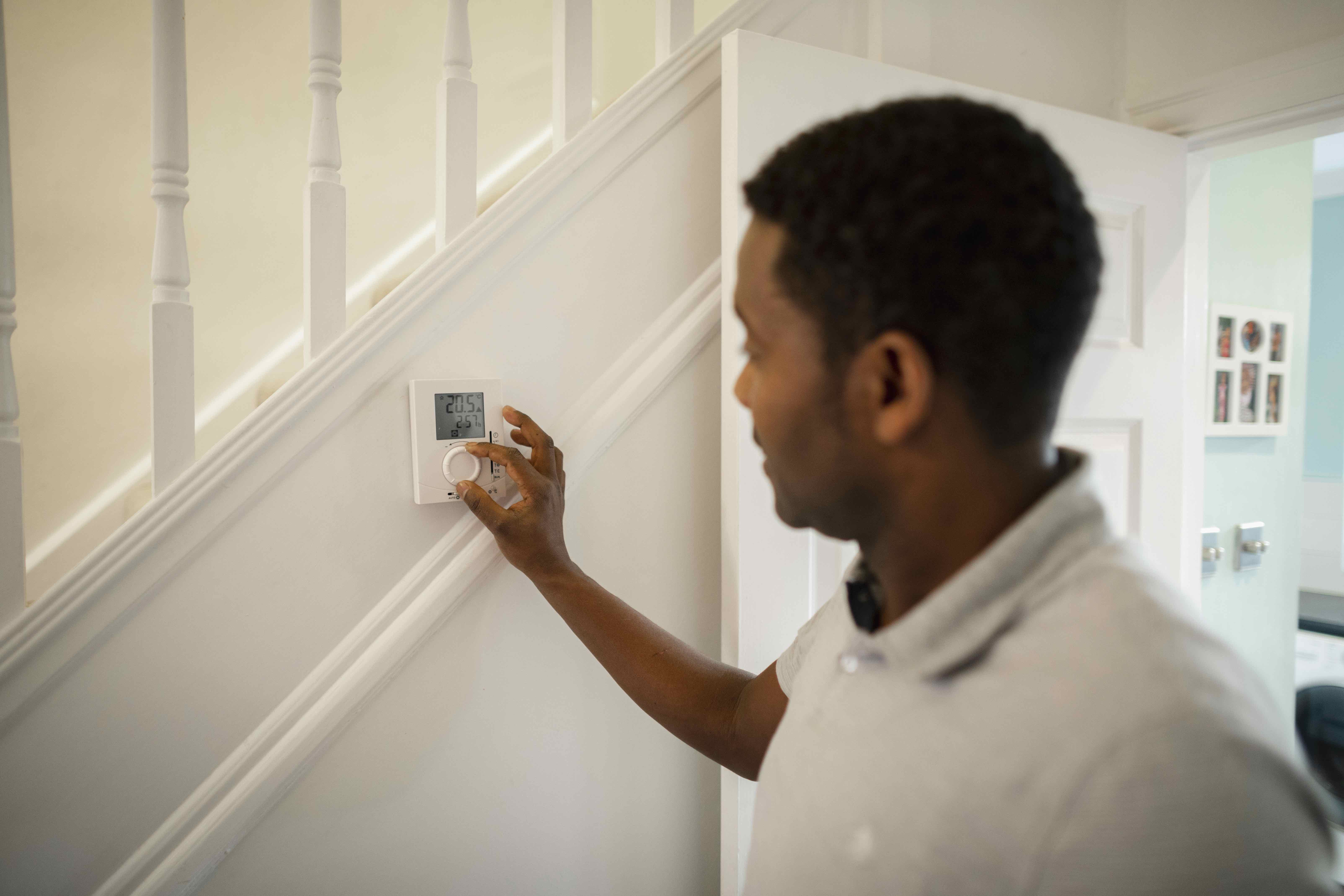 A man adjusts a thermostat inside a house