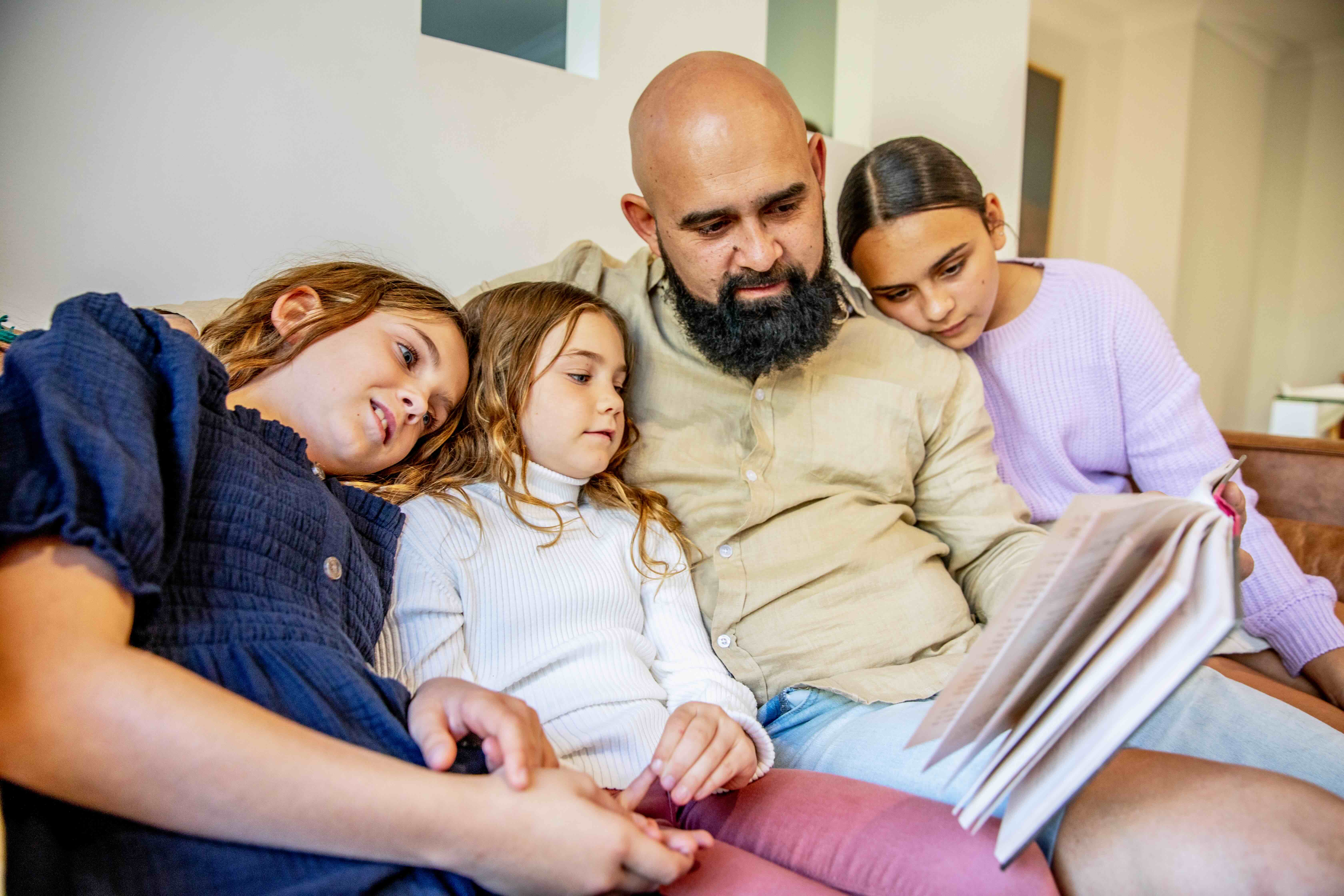 An Indigenous father reading to his daughters