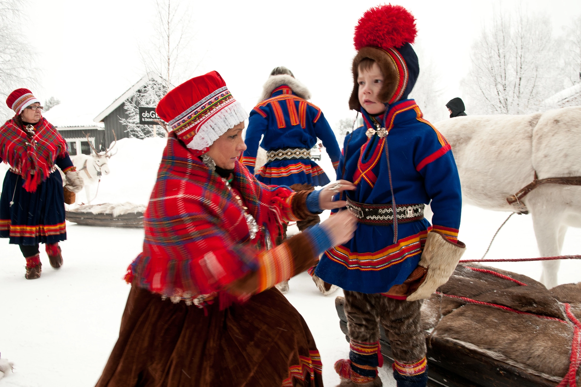 Sami woman clothing a young boy in traditional Sami dress