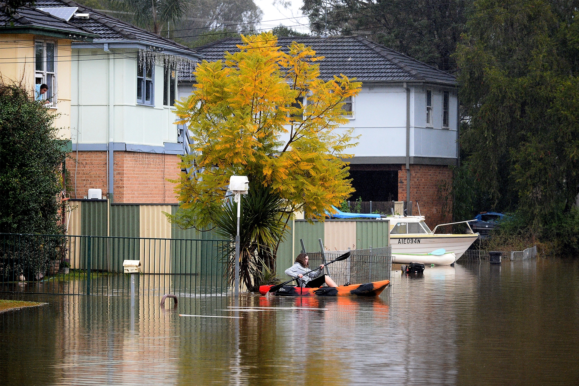 Woman kayaking past houses in a flooded suburban street