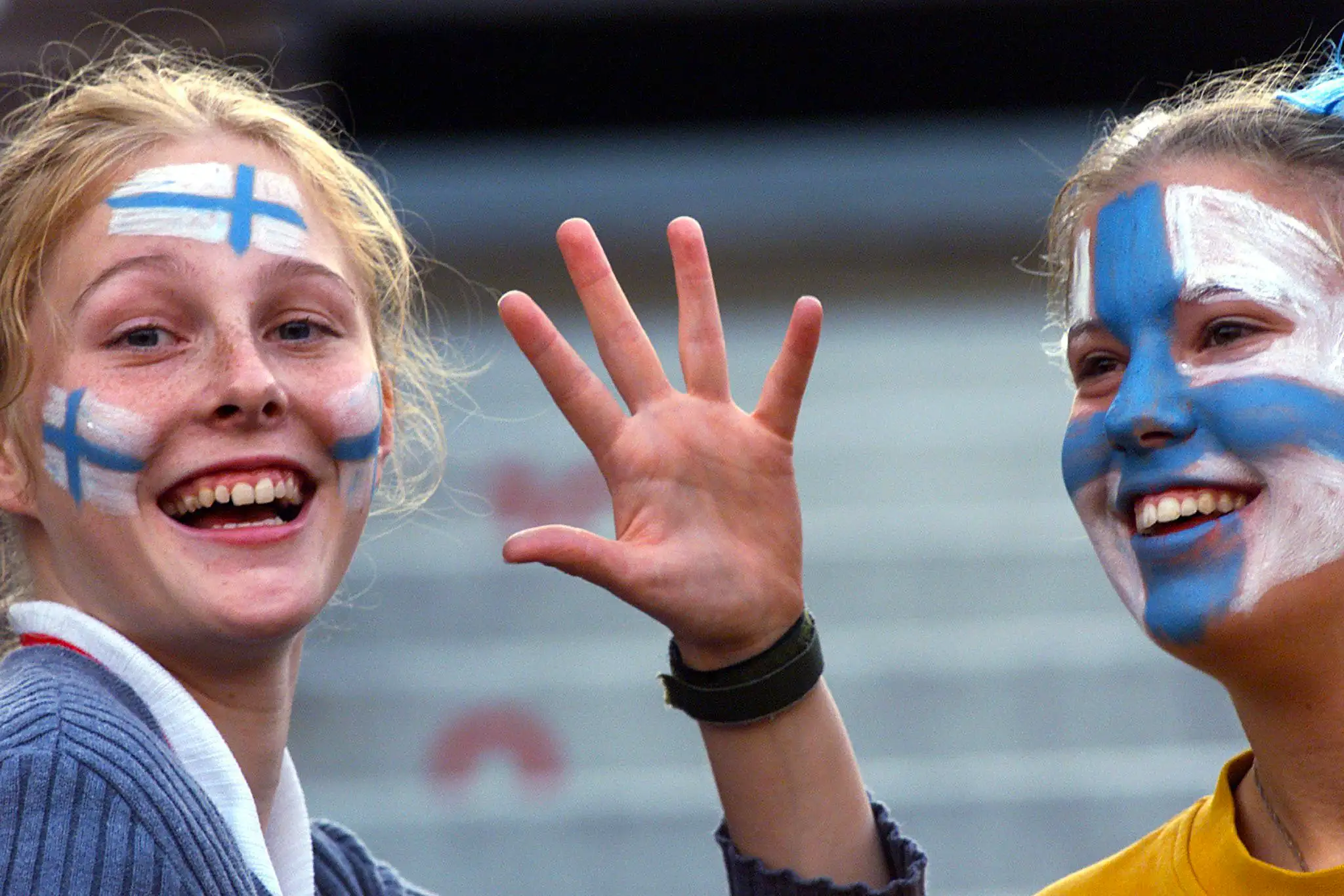 Two Finnish girls with flags painted on their faces wave at the camera