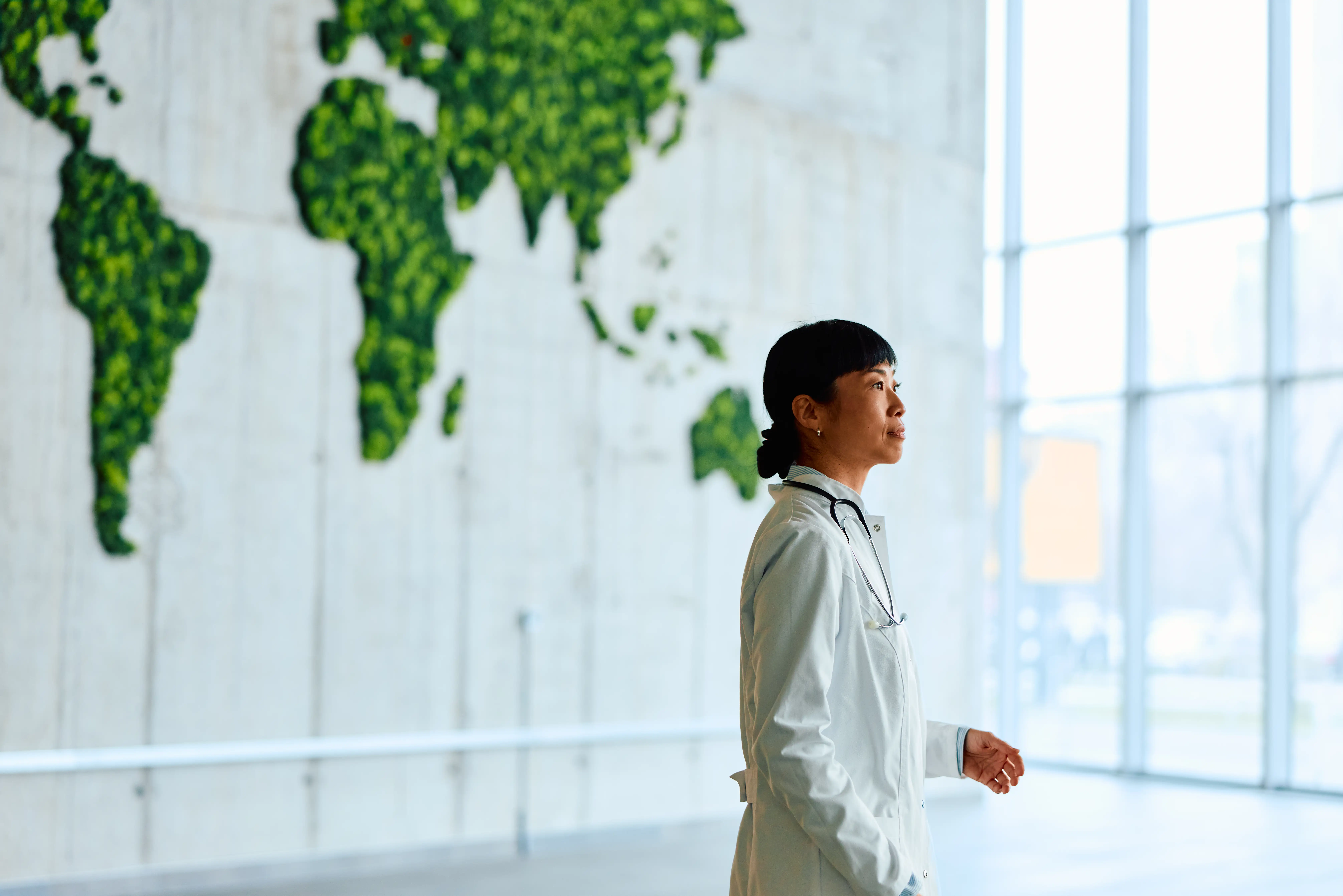 A female doctor stands in front of a large green world map featuring Australia