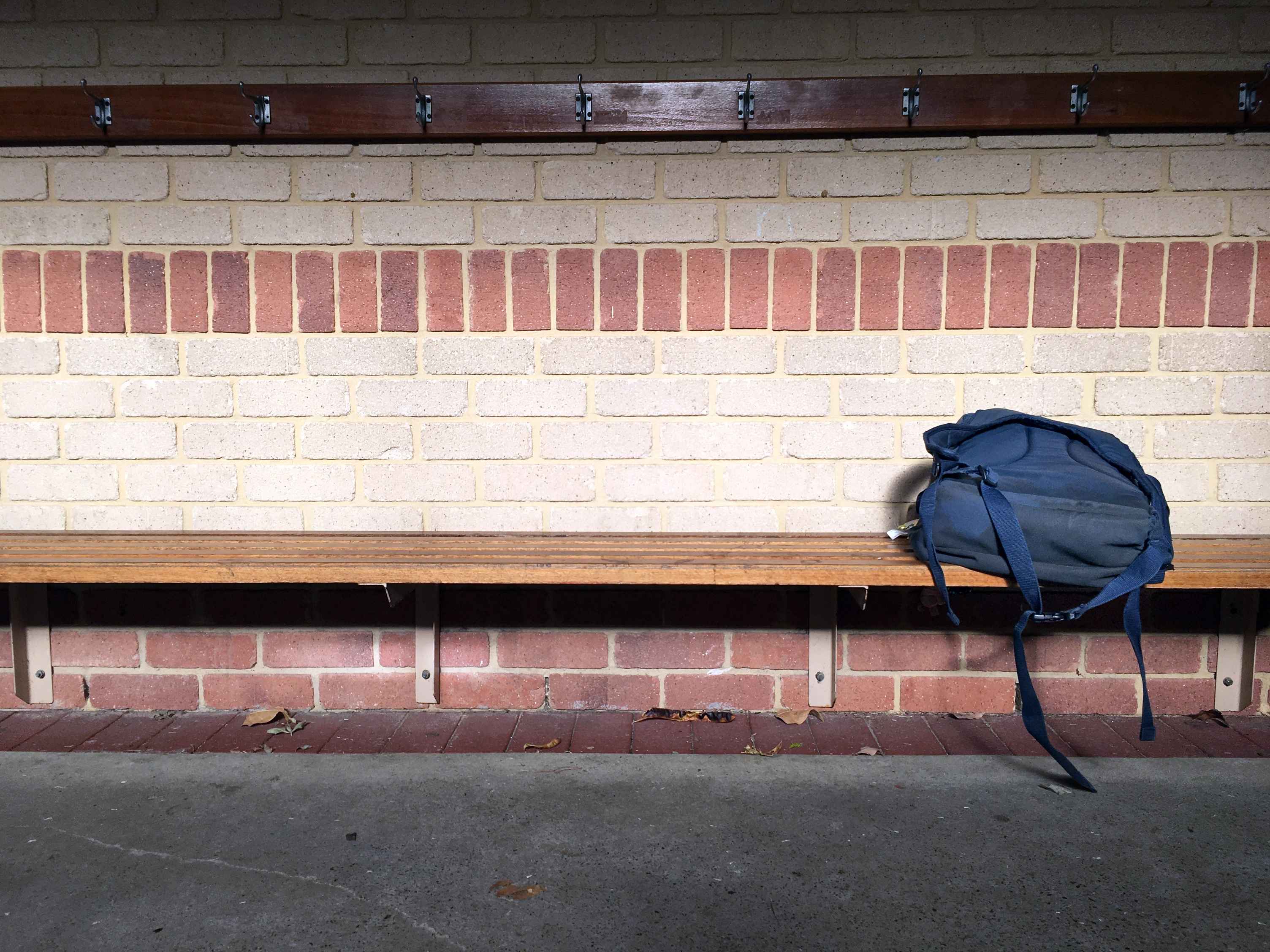 A blue school bag left on a long timber bench on the outside of a school