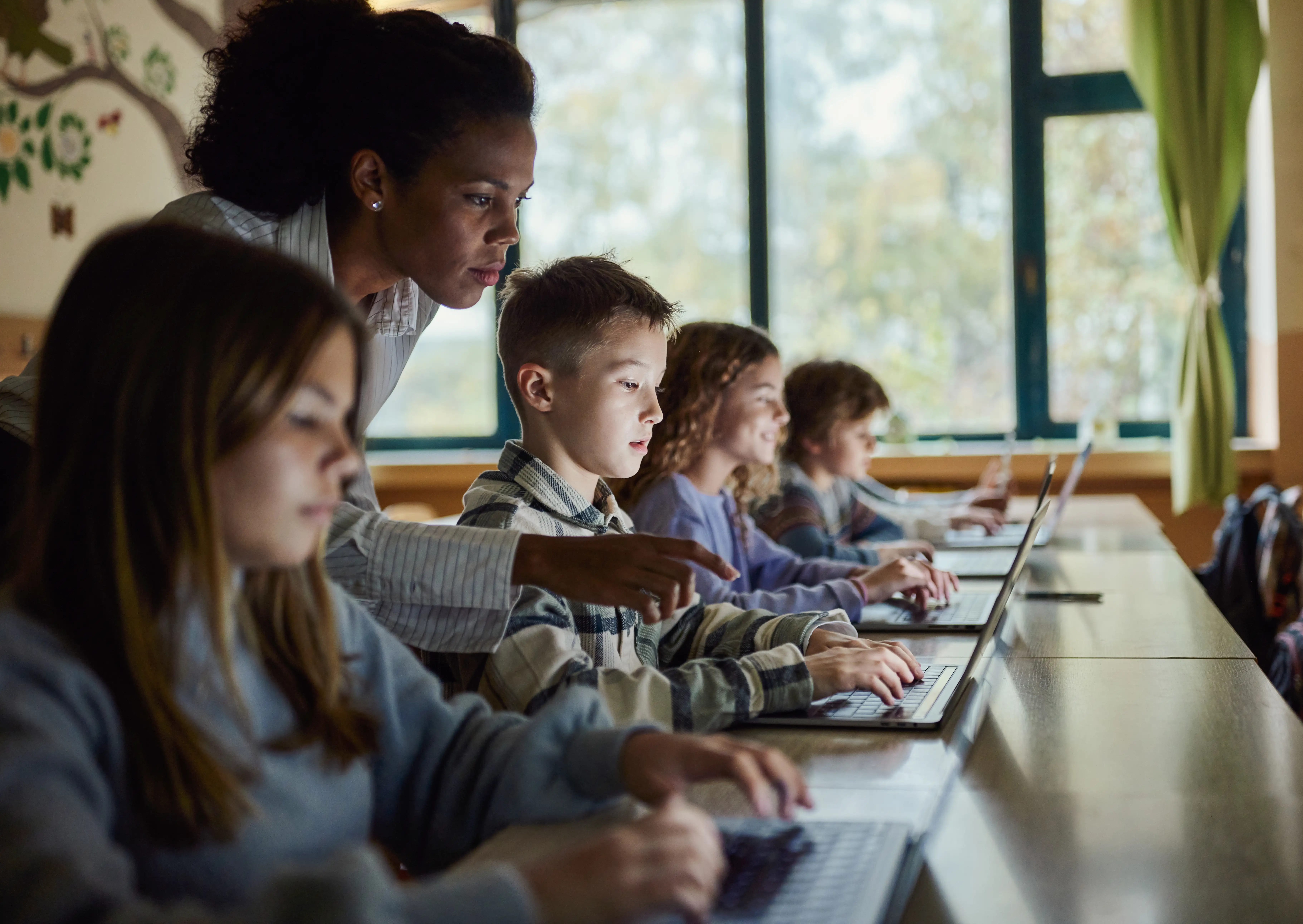 A female teacher assisting school kids during an e-learning class at primary school