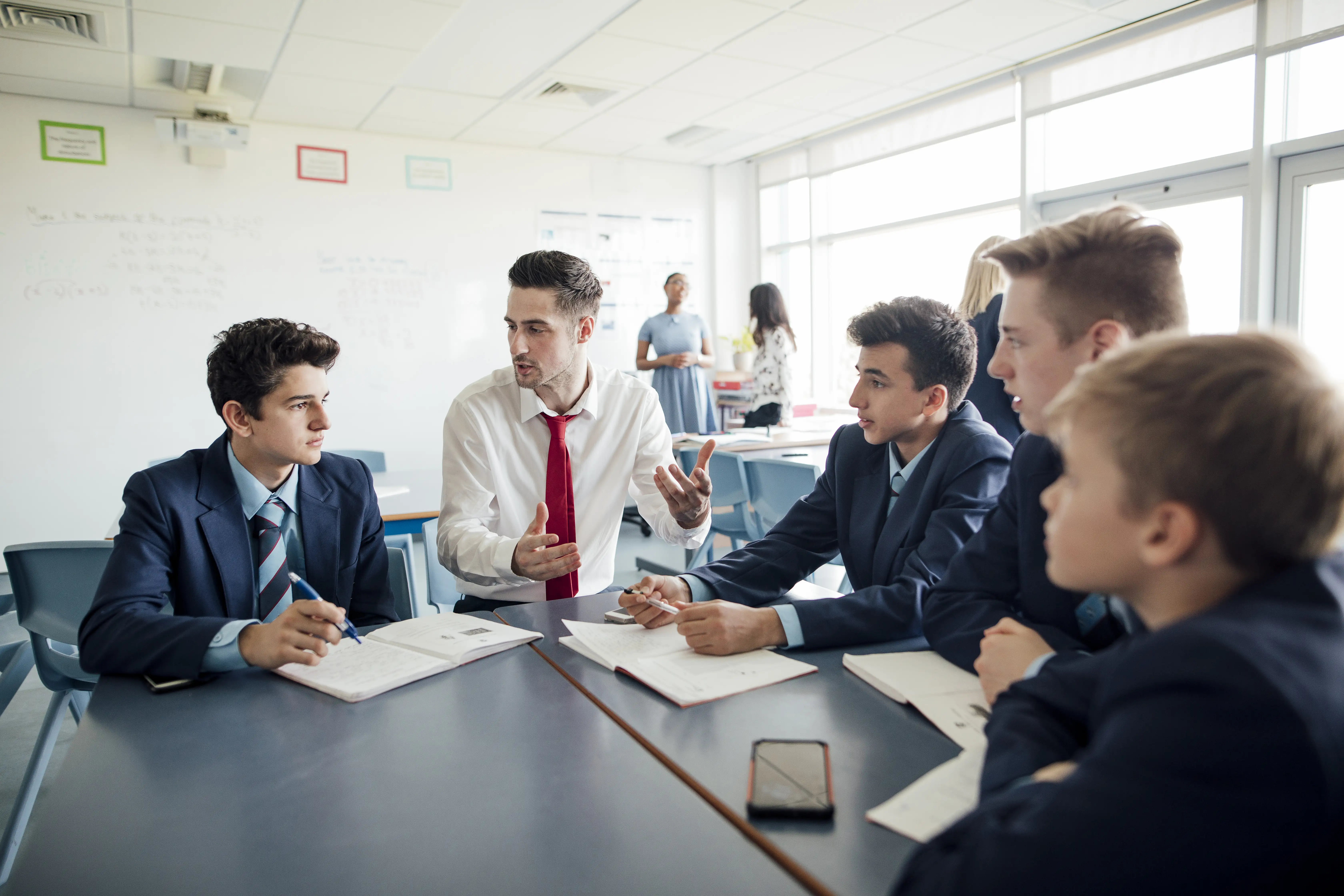 A teacher talks to a group of students working on a project in a classroom