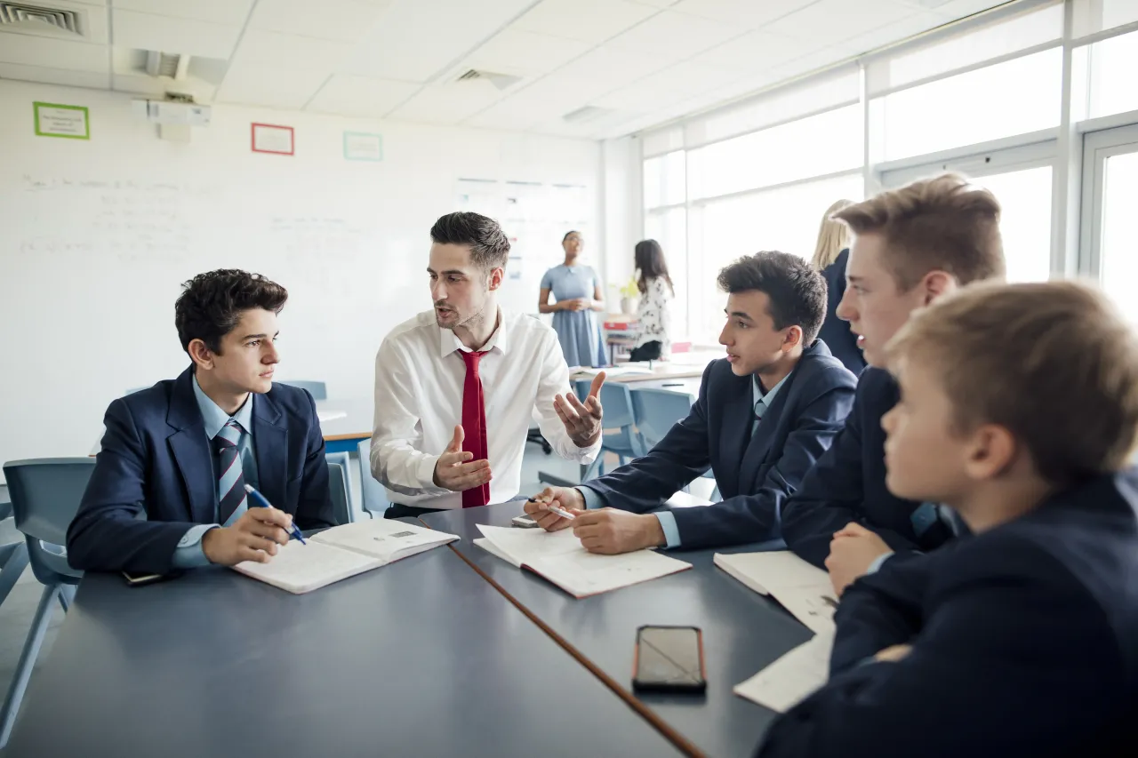 A teacher talks to a group of students working on a project in a classroom