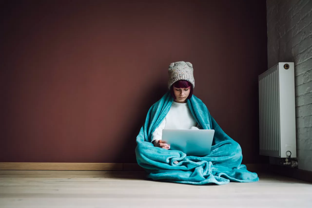 A young woman in a blanket near a heater