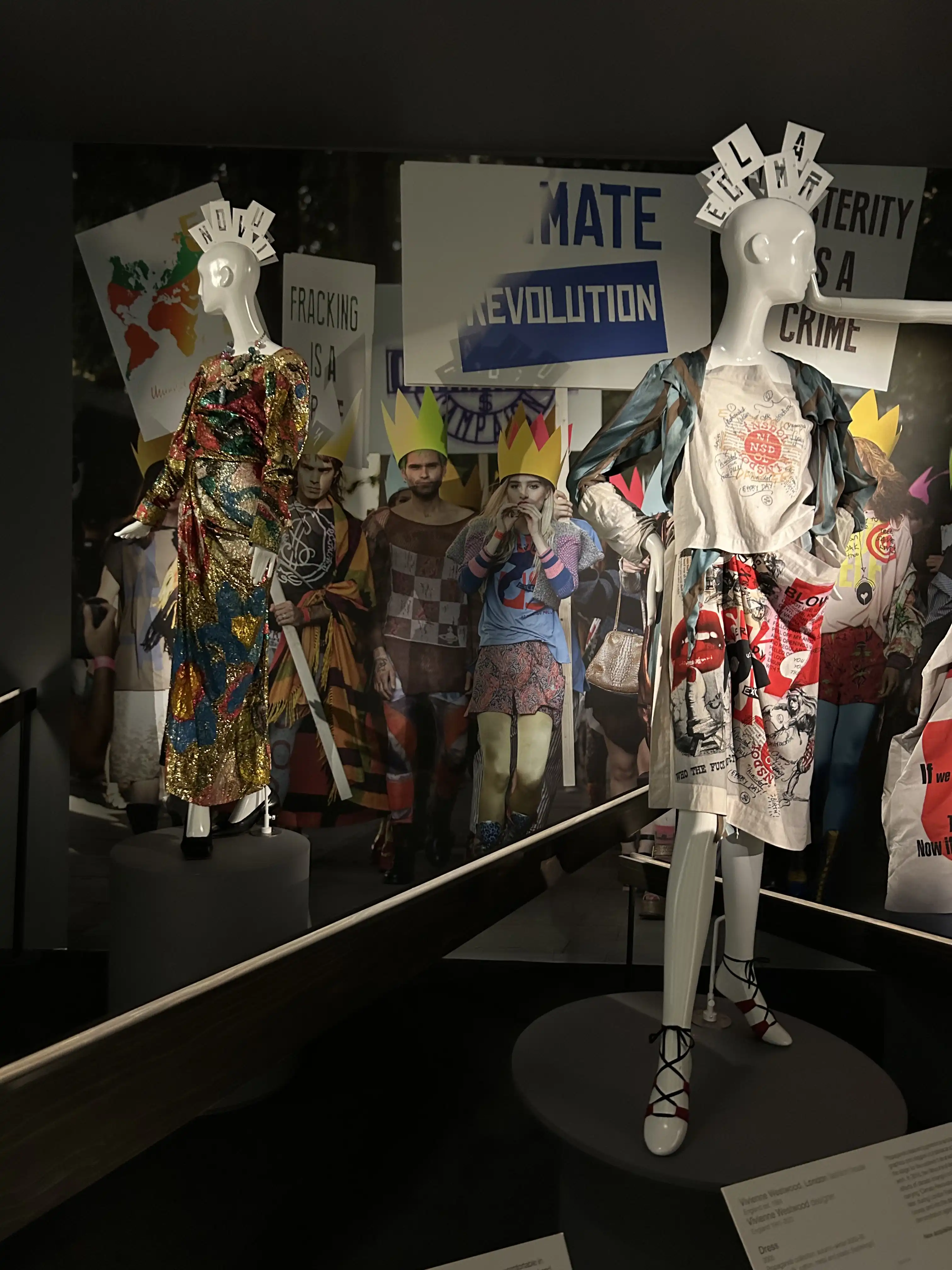 Two Westwood designed outfits covered in political imagery in front of a backdrop of climate protesters