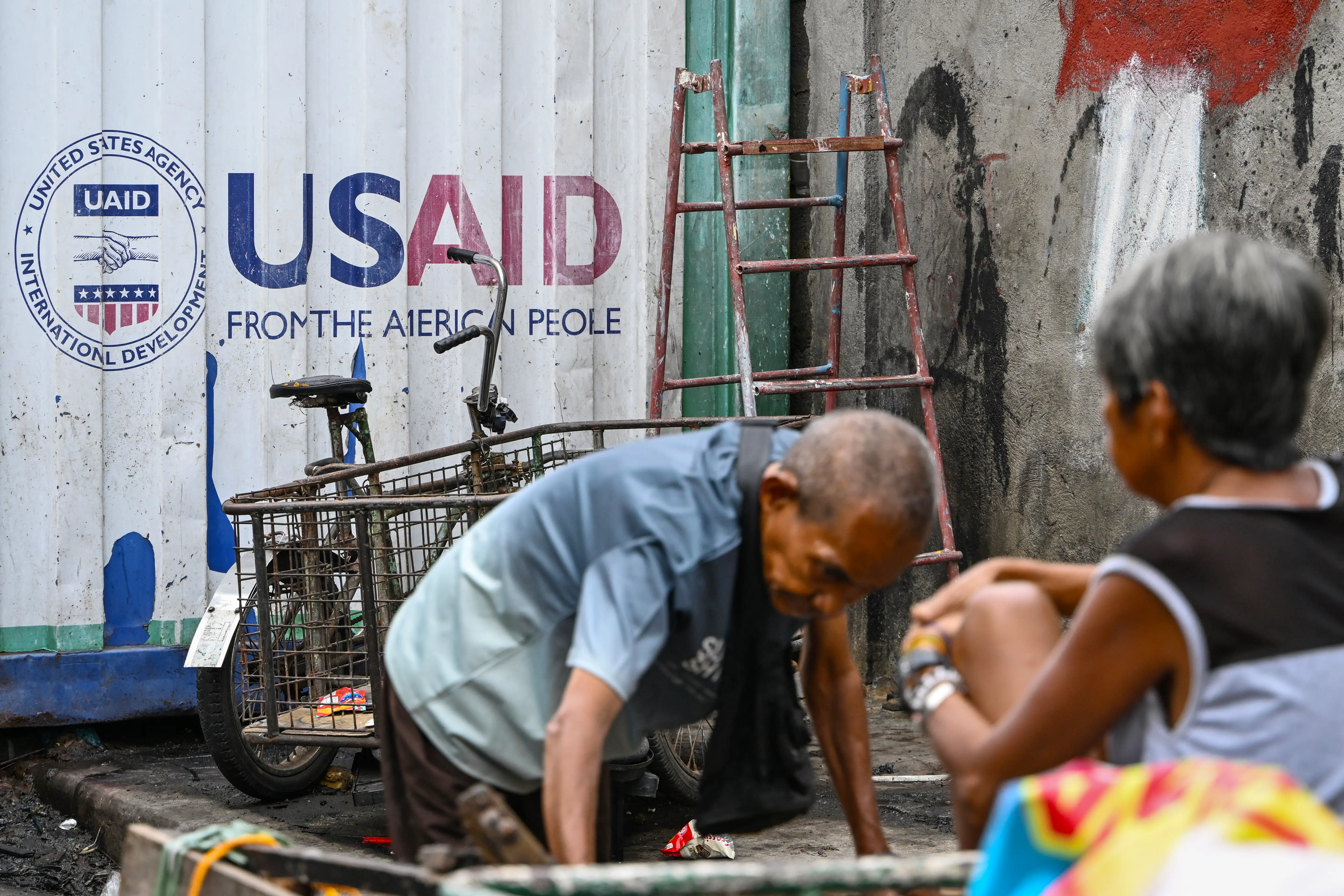 Signage for the US government's humanitarian agency USAID behind people sorting through junk in Manila.