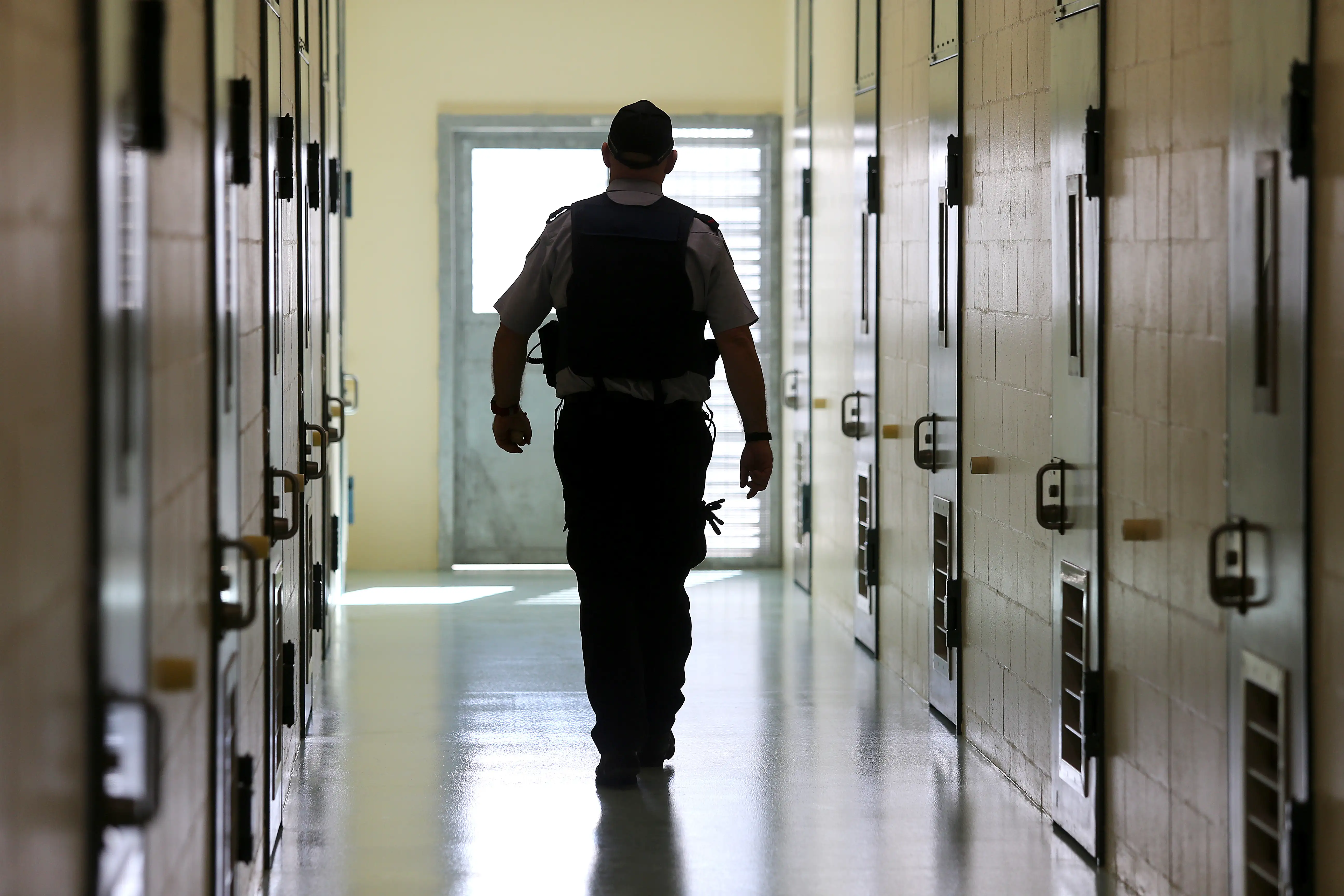 A corrections officer walks down a cell corridor.