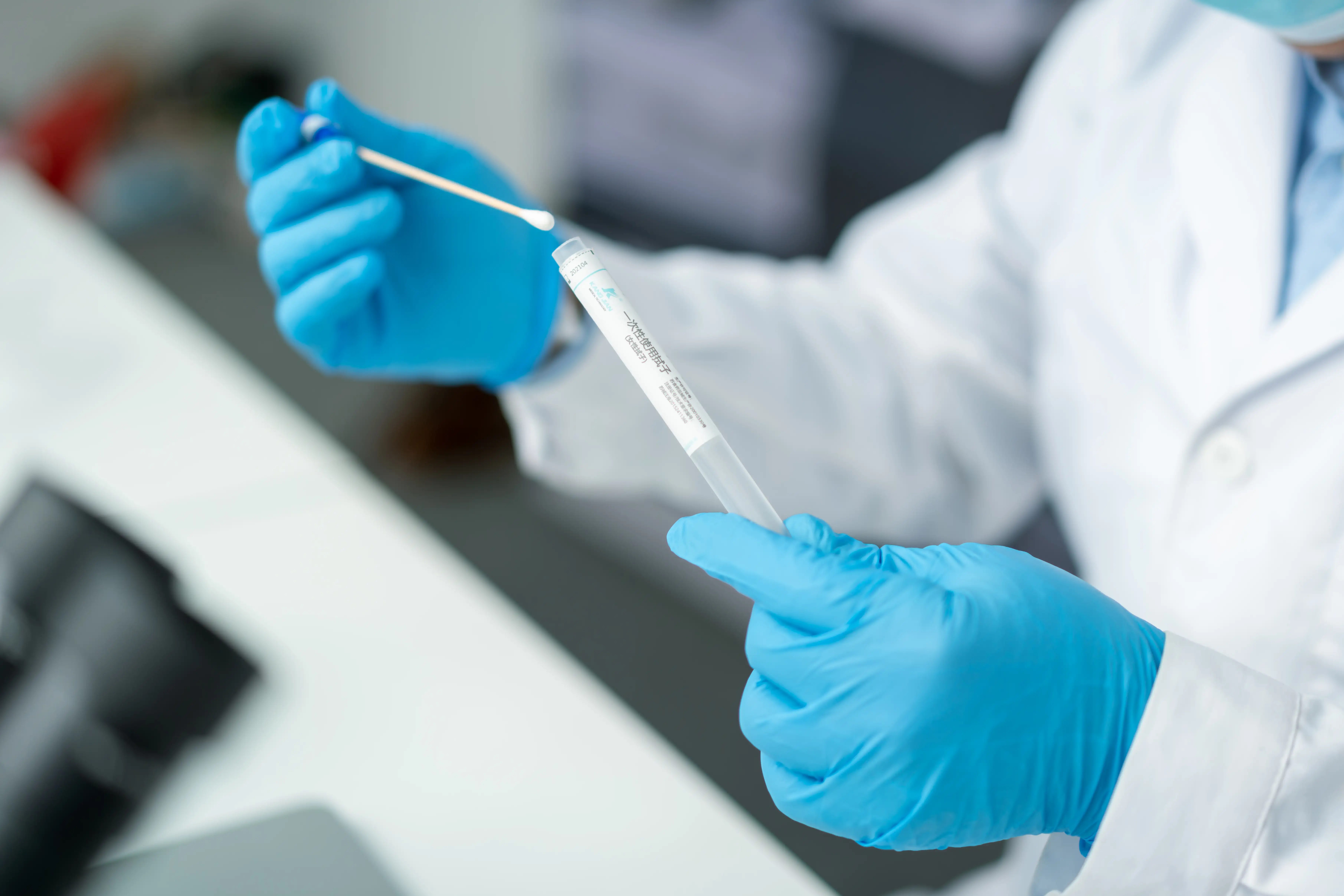 A pair of gloved hands hold a swab in a lab