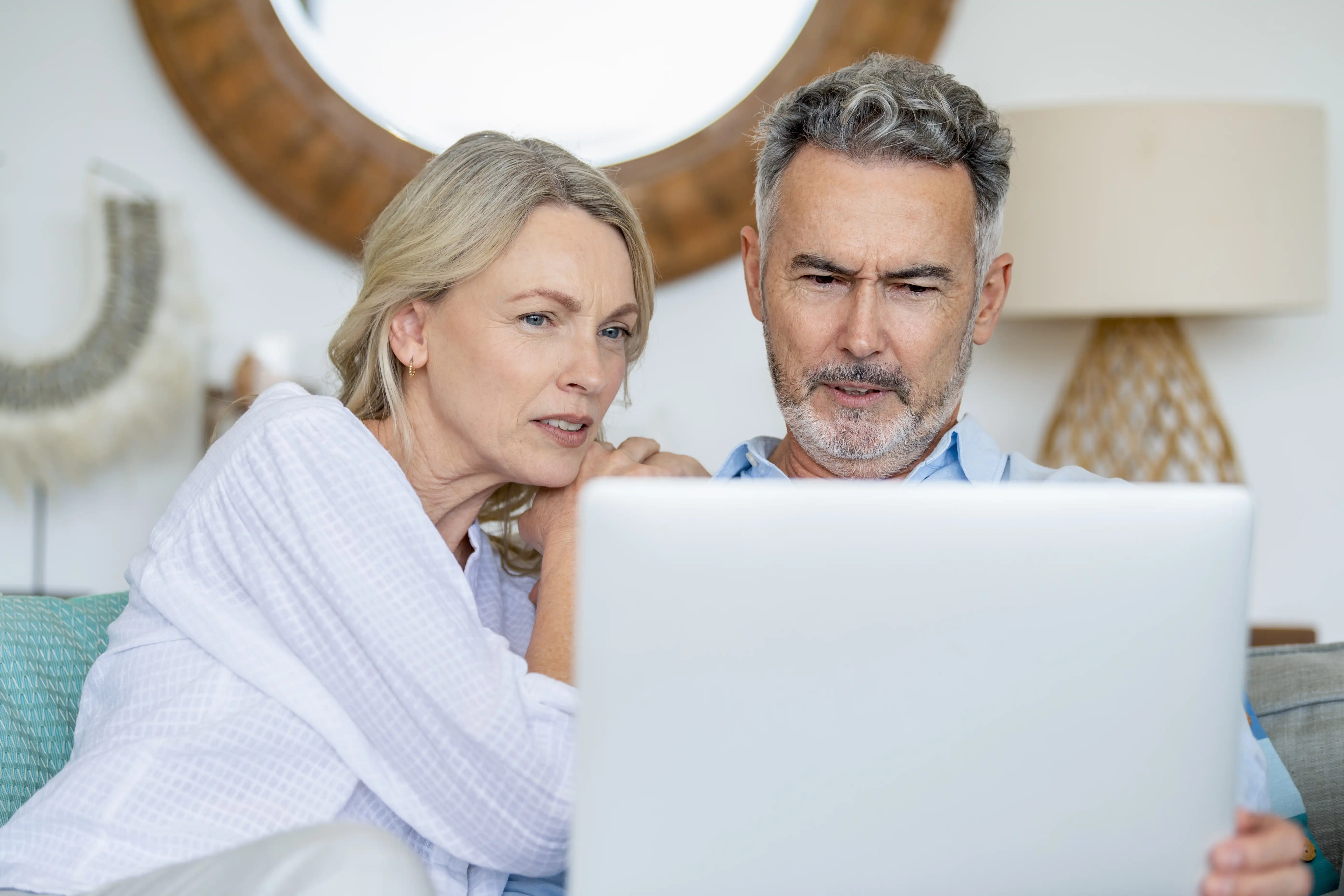 An older couple sit on a couch together studying a laptop screen