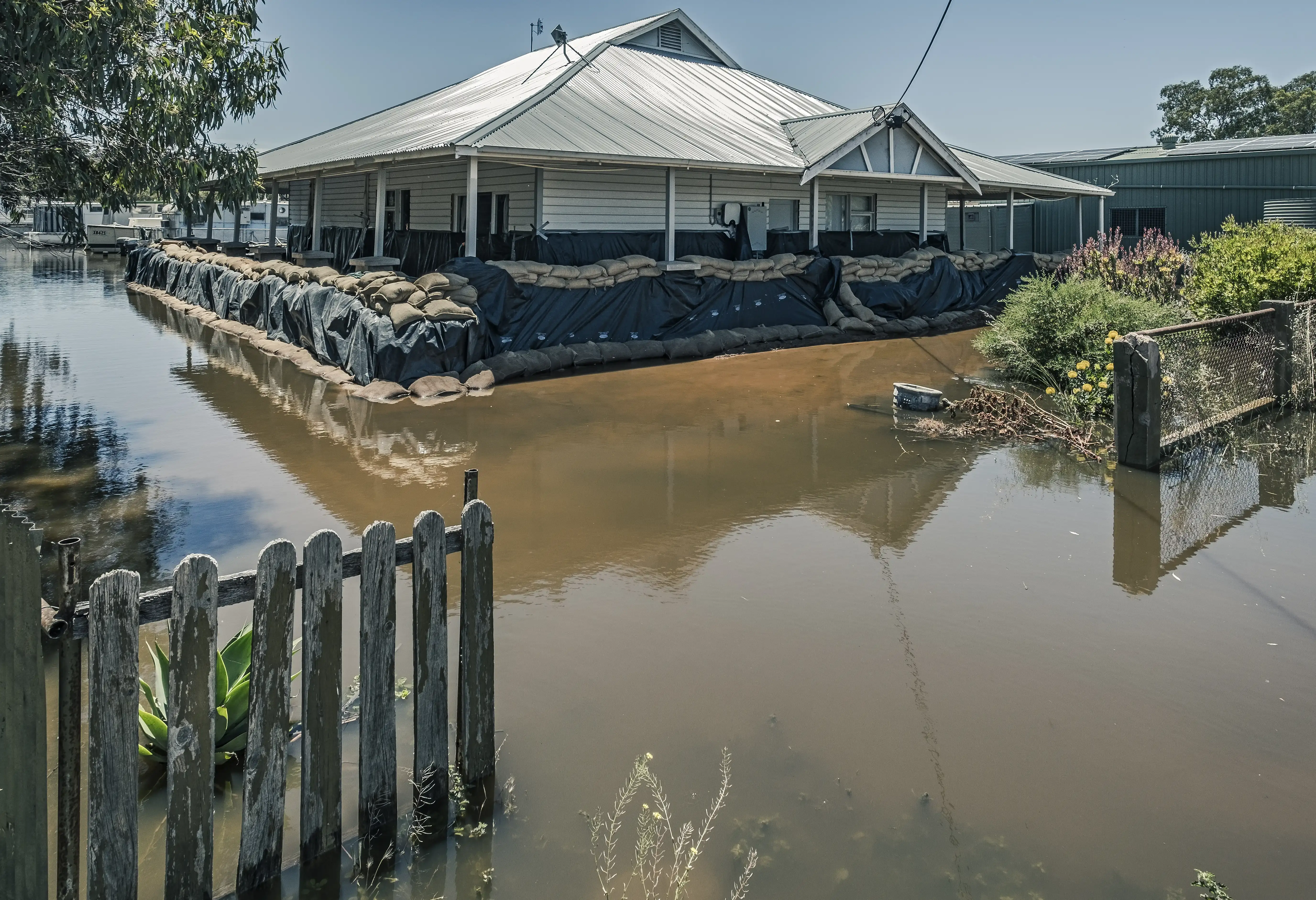 A weatherboard home is surrounded by floodwaters, with sandbags stacked around the house.