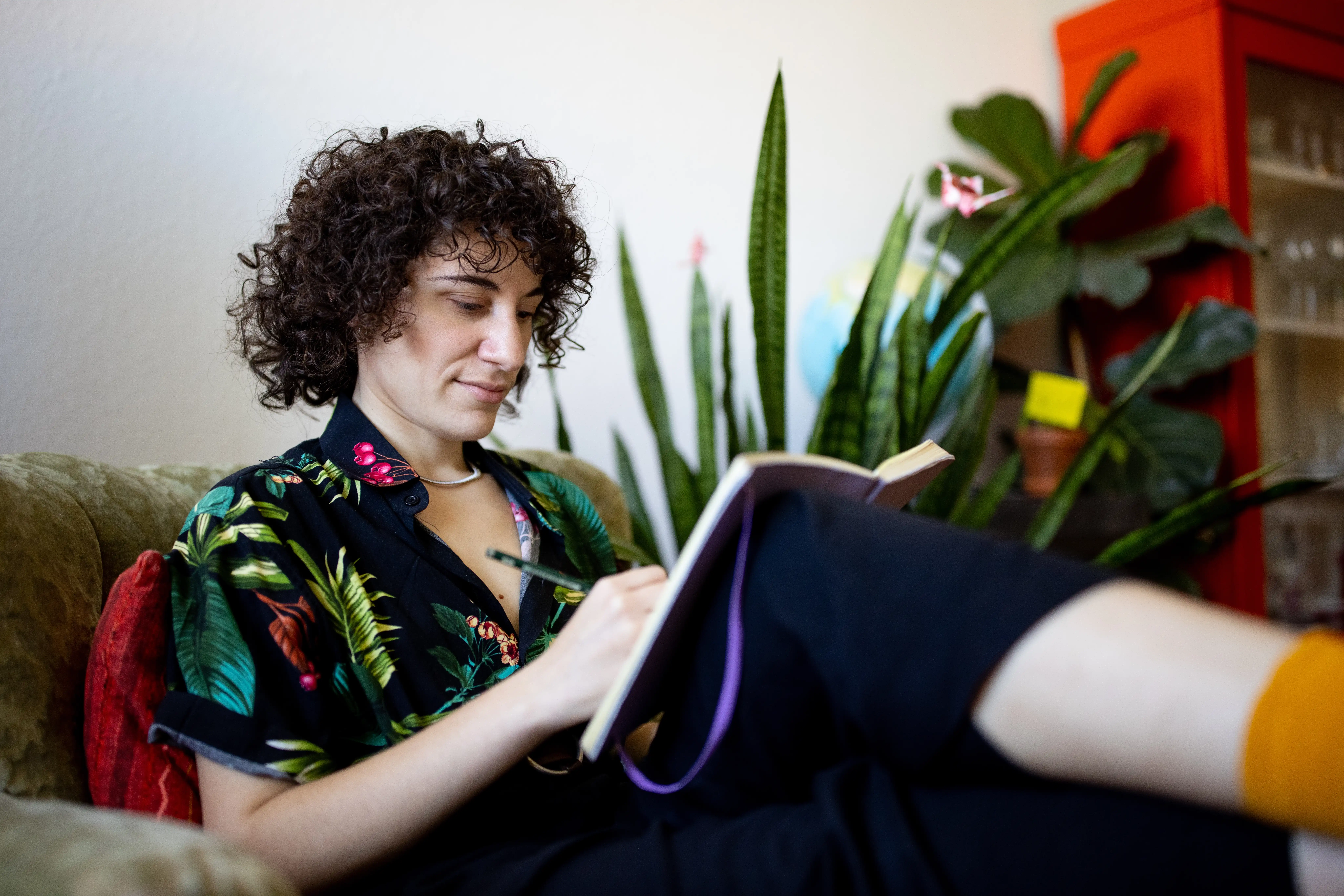 A non-binary person sitting in a chair writing in a notebook