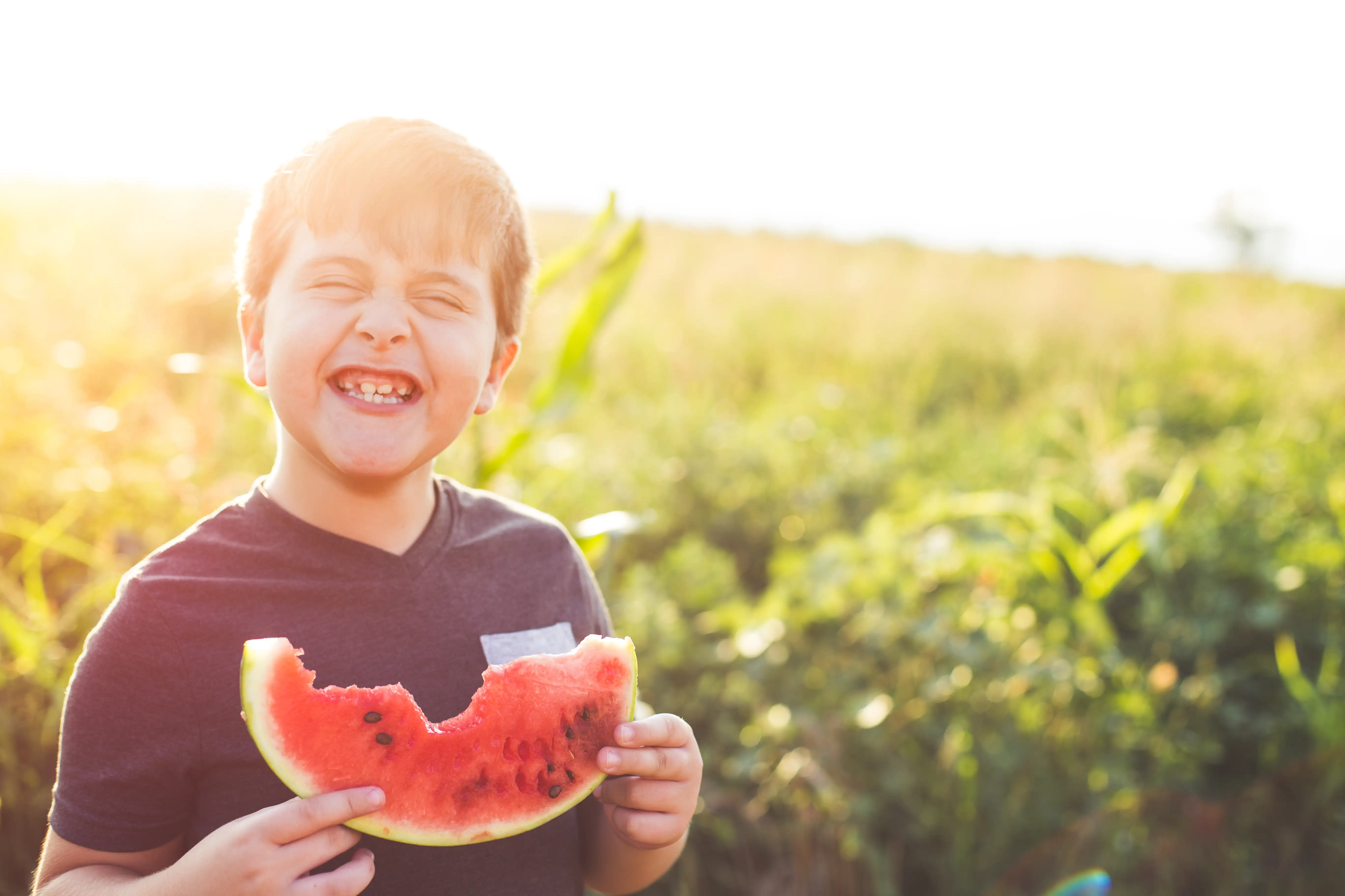 A boy smiling while eating watermelon