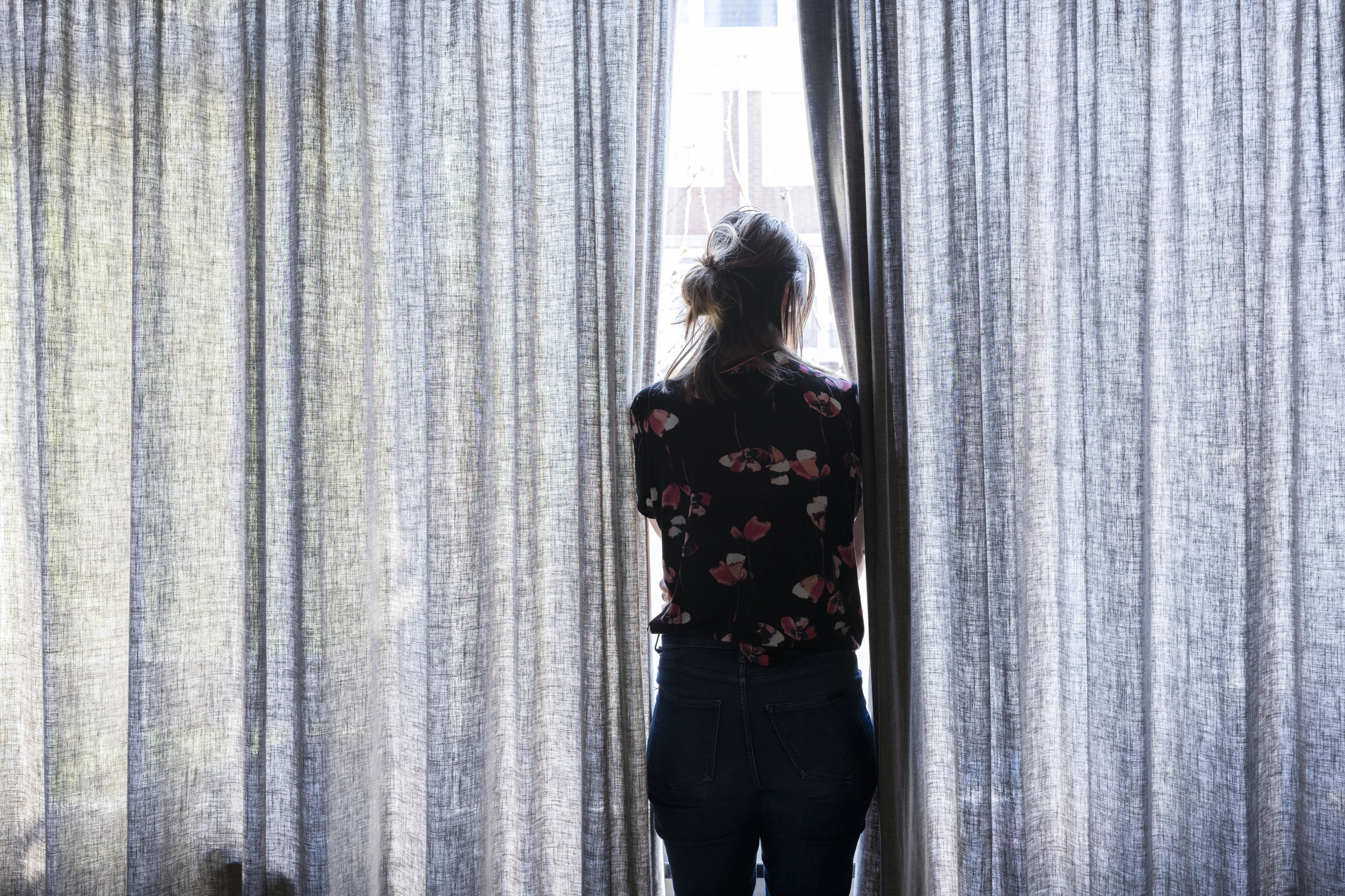 A woman standing between closed curtains at a window.