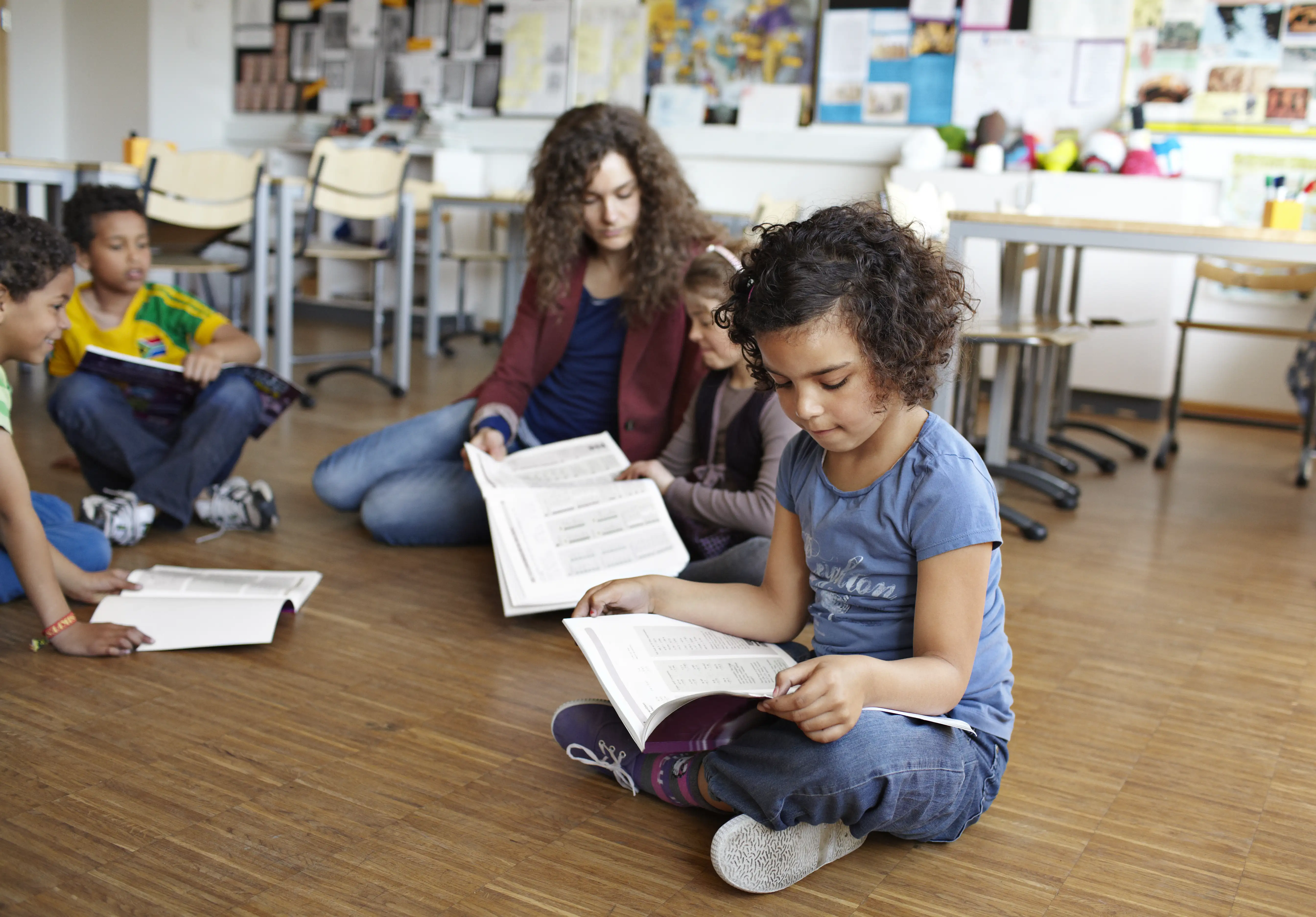 A primary schoolgirl reading in the classroom sitting on the floor