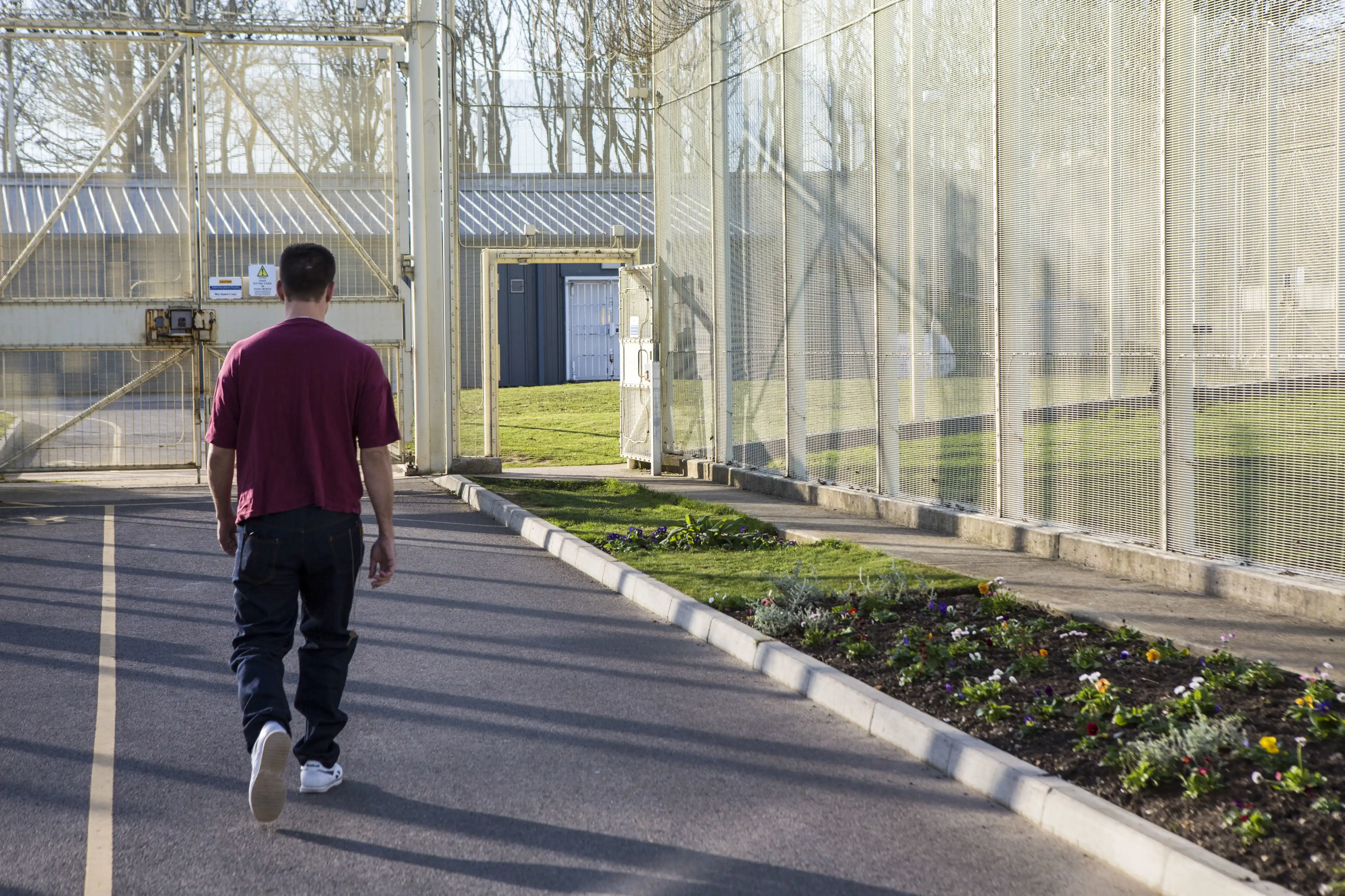 A man walks towards an exit of a fence-lined courtyard in prison