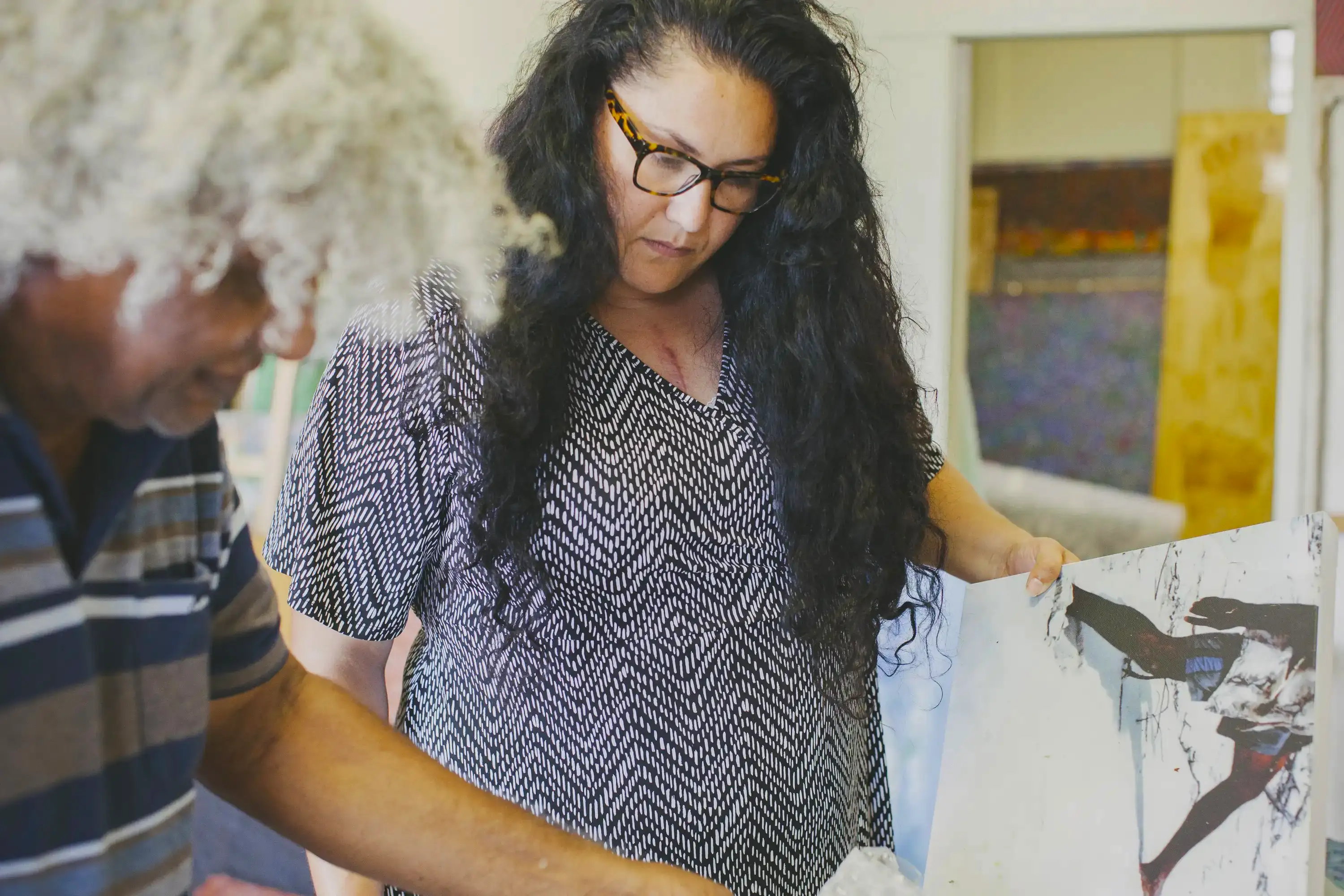 An Indigenous woman inspects artwork in an Indigenous artist's studio