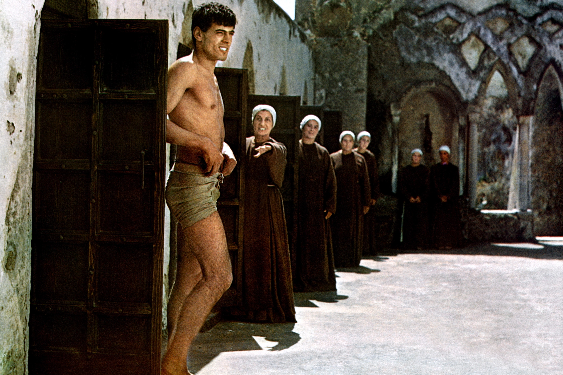 Film still showing man in loincloth being looked at by a group of women