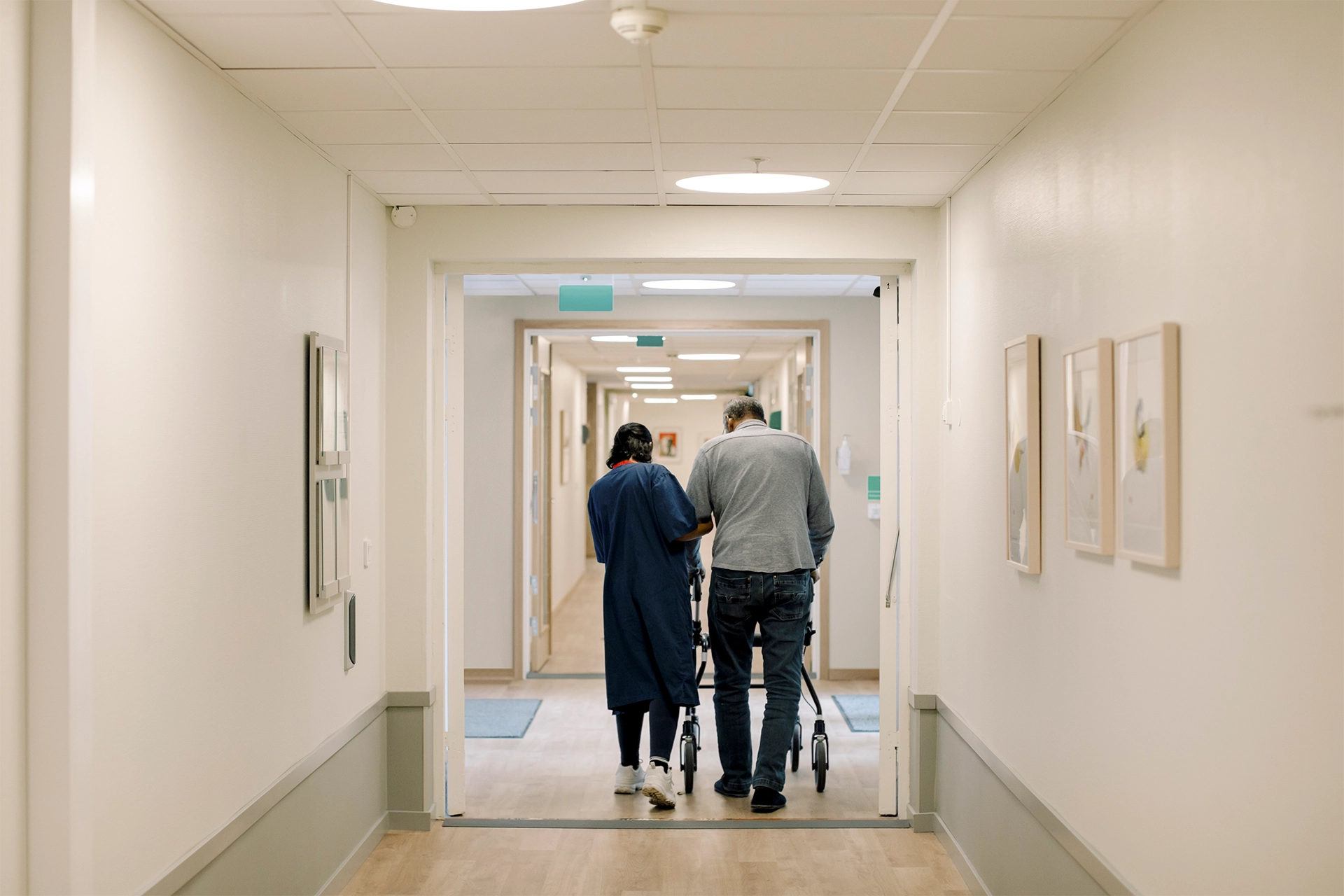 A nurse guides an elderly man through a hospital hallway