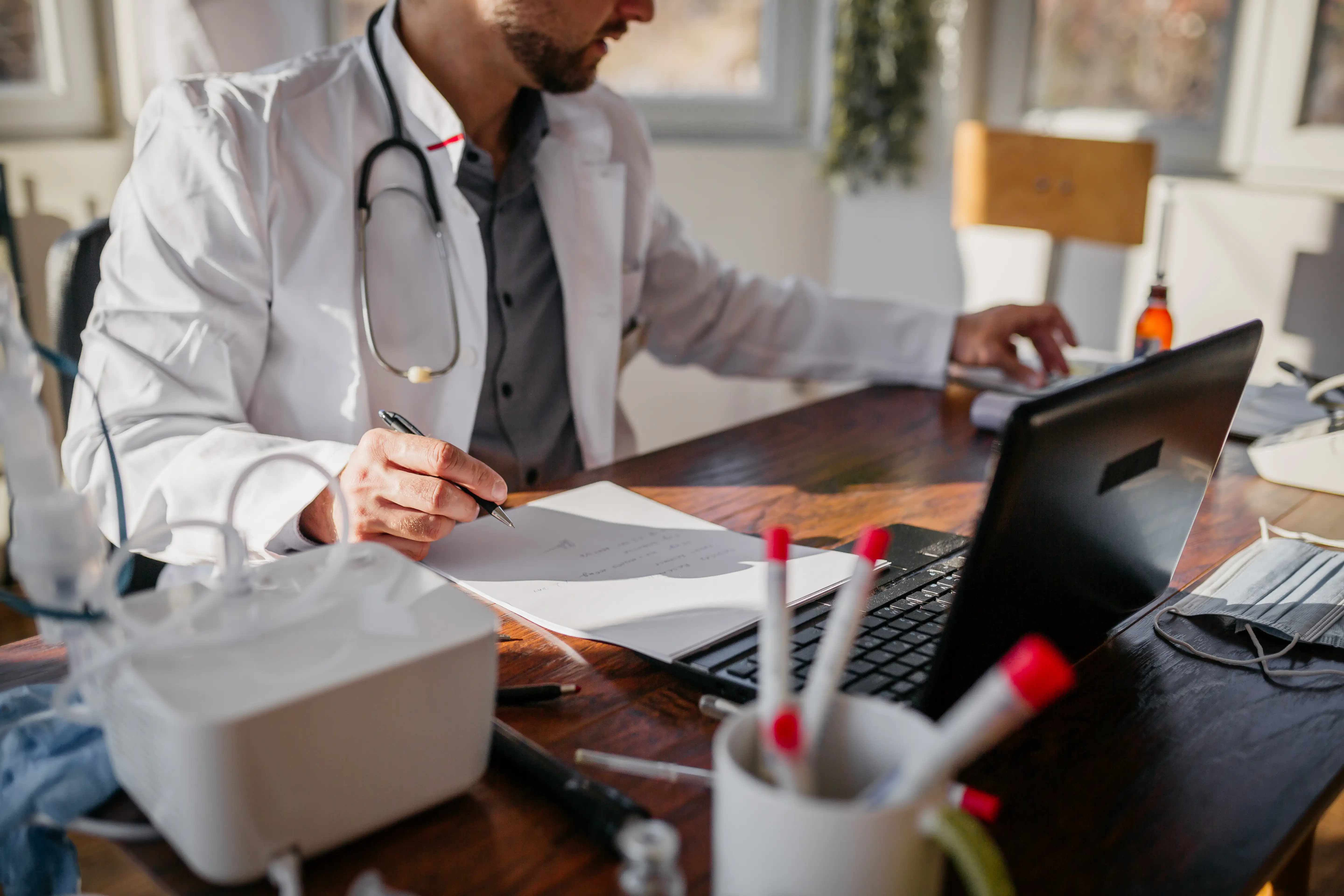 A busy male doctor completes paperwork at his desk