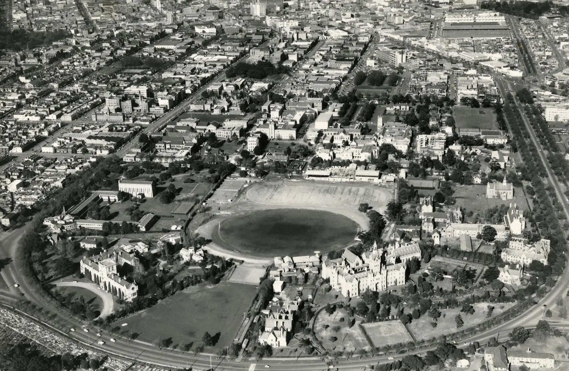 Aerial view showing beyond the main oval, the new cinder track enclosing hockey and field athletics area, and the Beaurepaire Centre, c1956