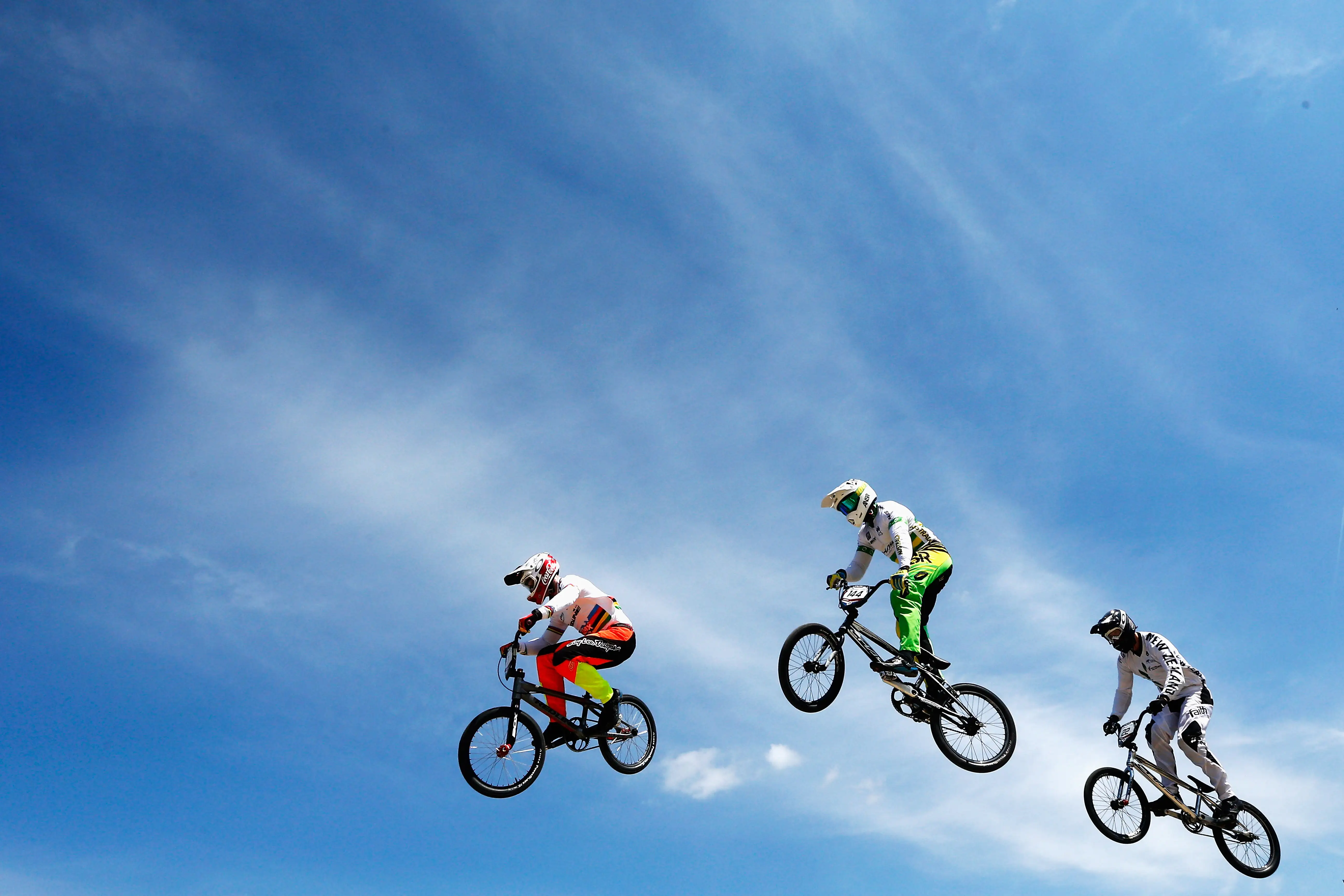 Three BMX riders go over a jump together