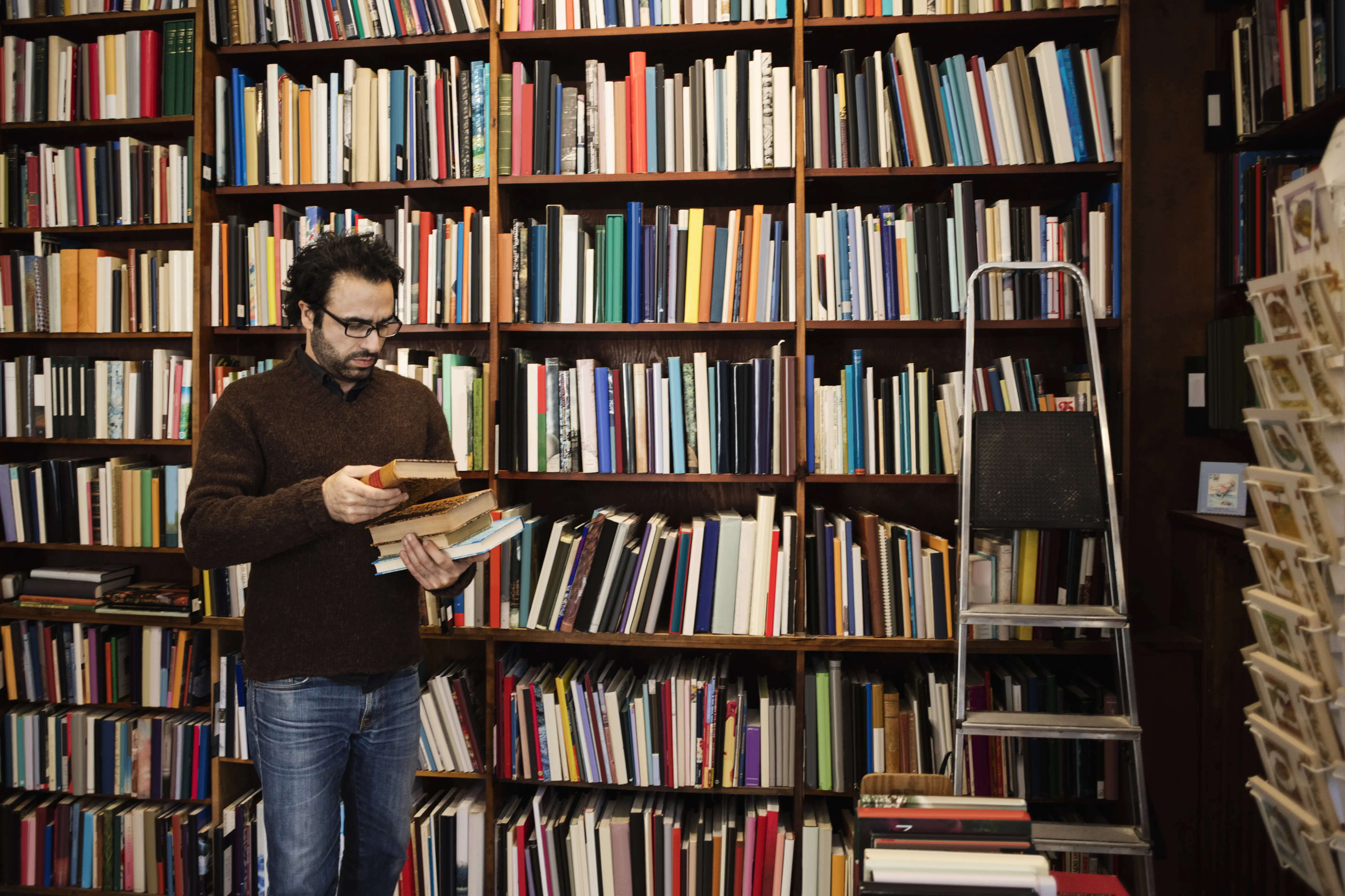 Man reading a book while standing against bookshelves