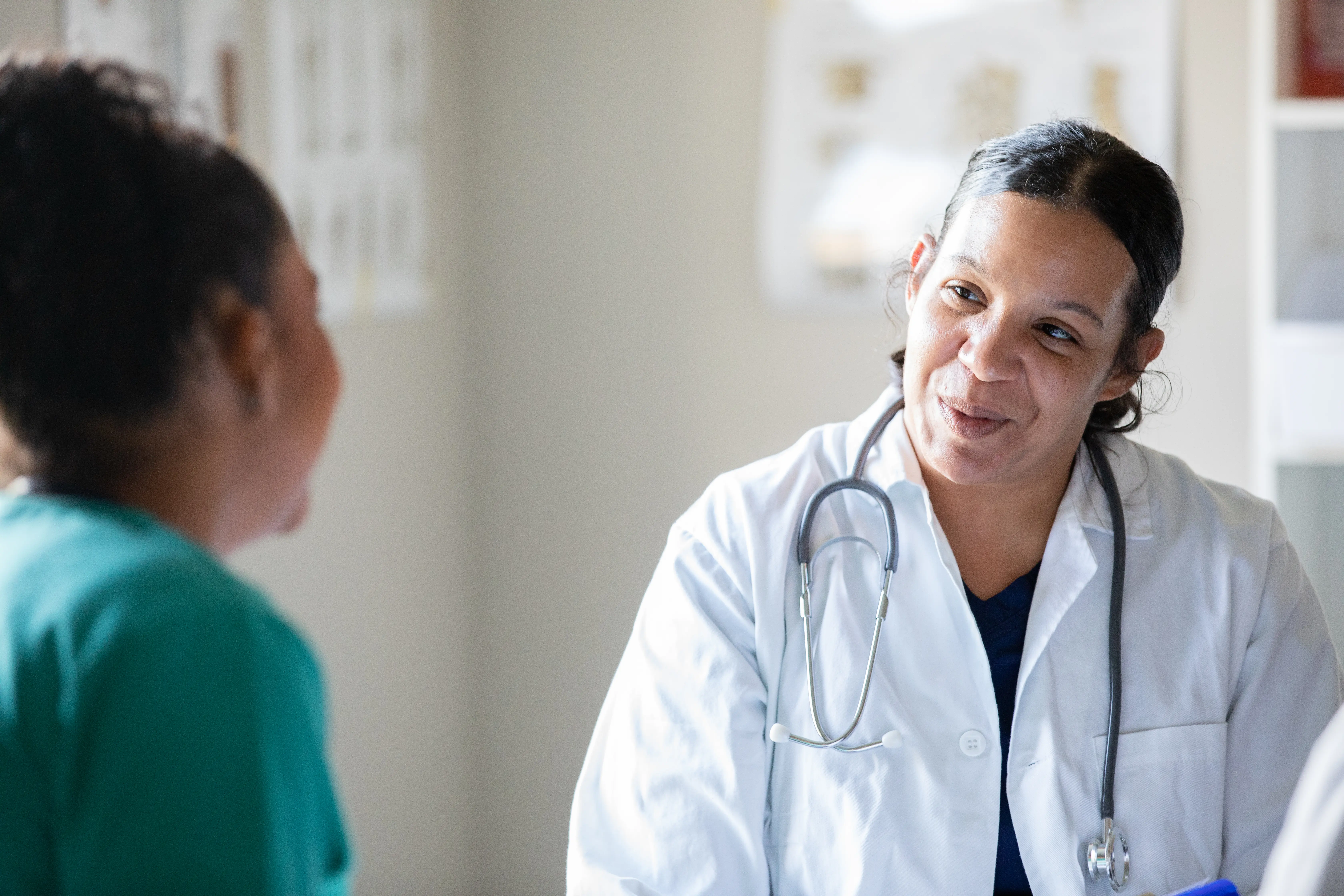 Mature doctor wearing white lab coat while speaking with a patient.