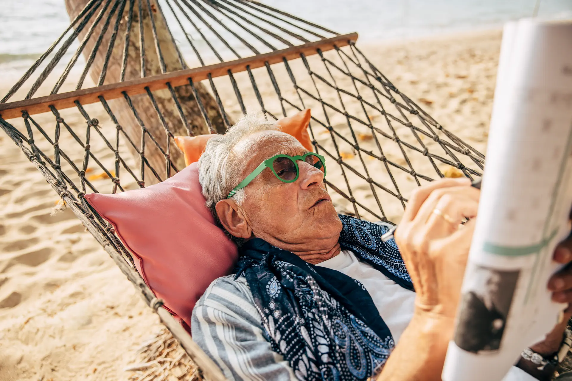 Elderly man doing a crossword while relaxing in a hammock on the beach