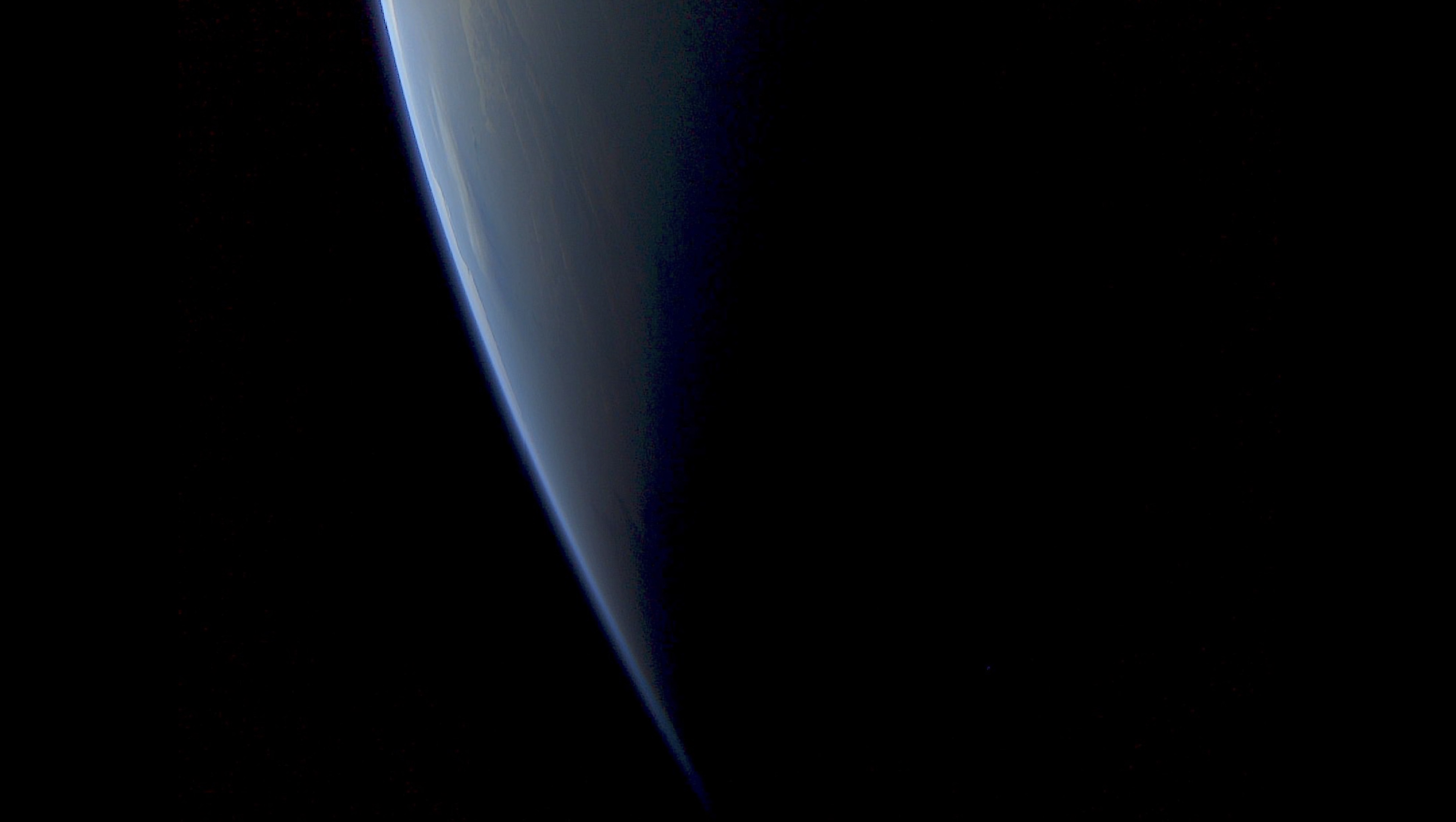 A dark Earth from space with a slither of light lighting its edge
